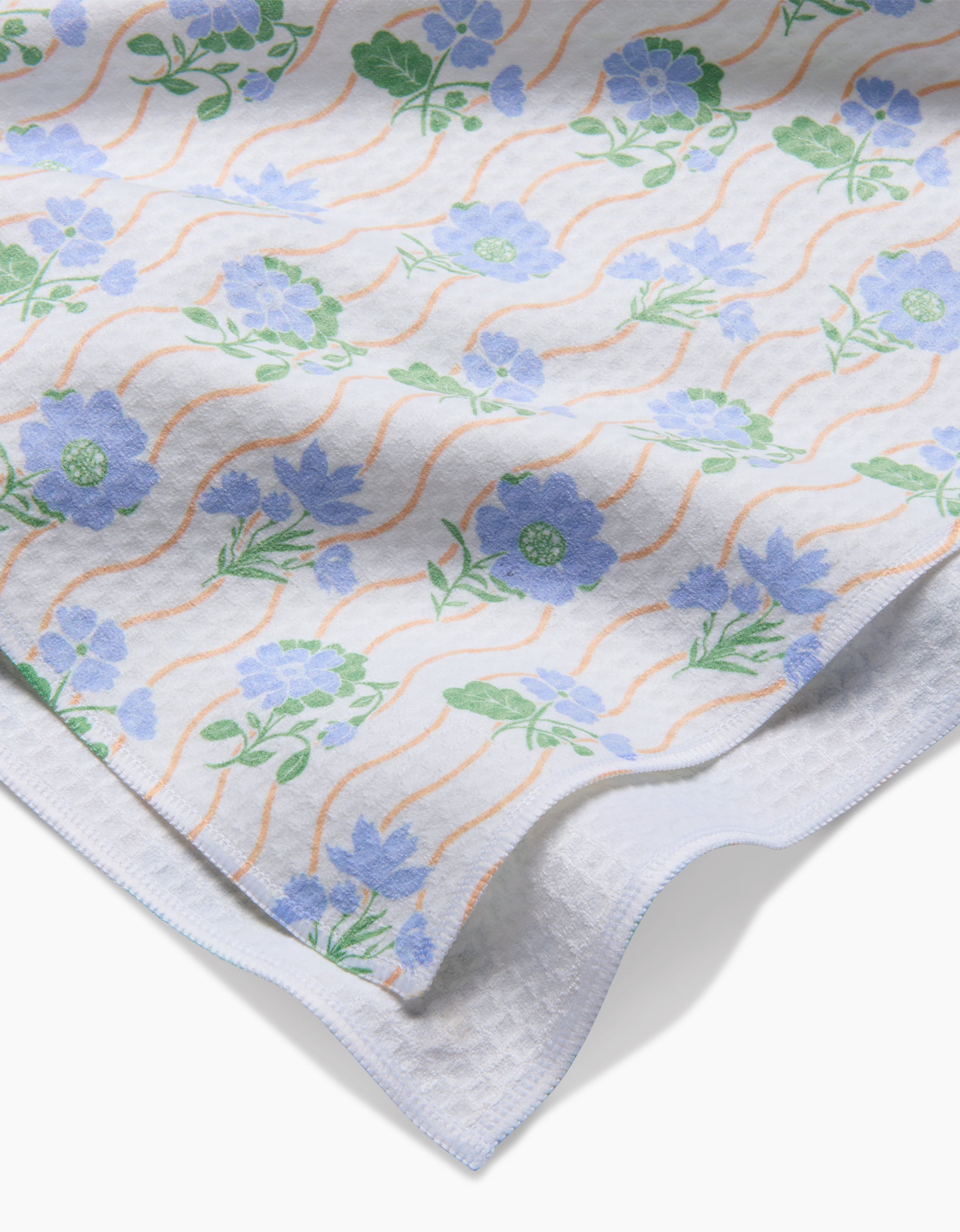 Spring Wave by Danelys Sidron—a white fabric with blue and green floral patterns and orange wavy lines, featuring quick-drying Geoweave technology—draped over a textured white surface.