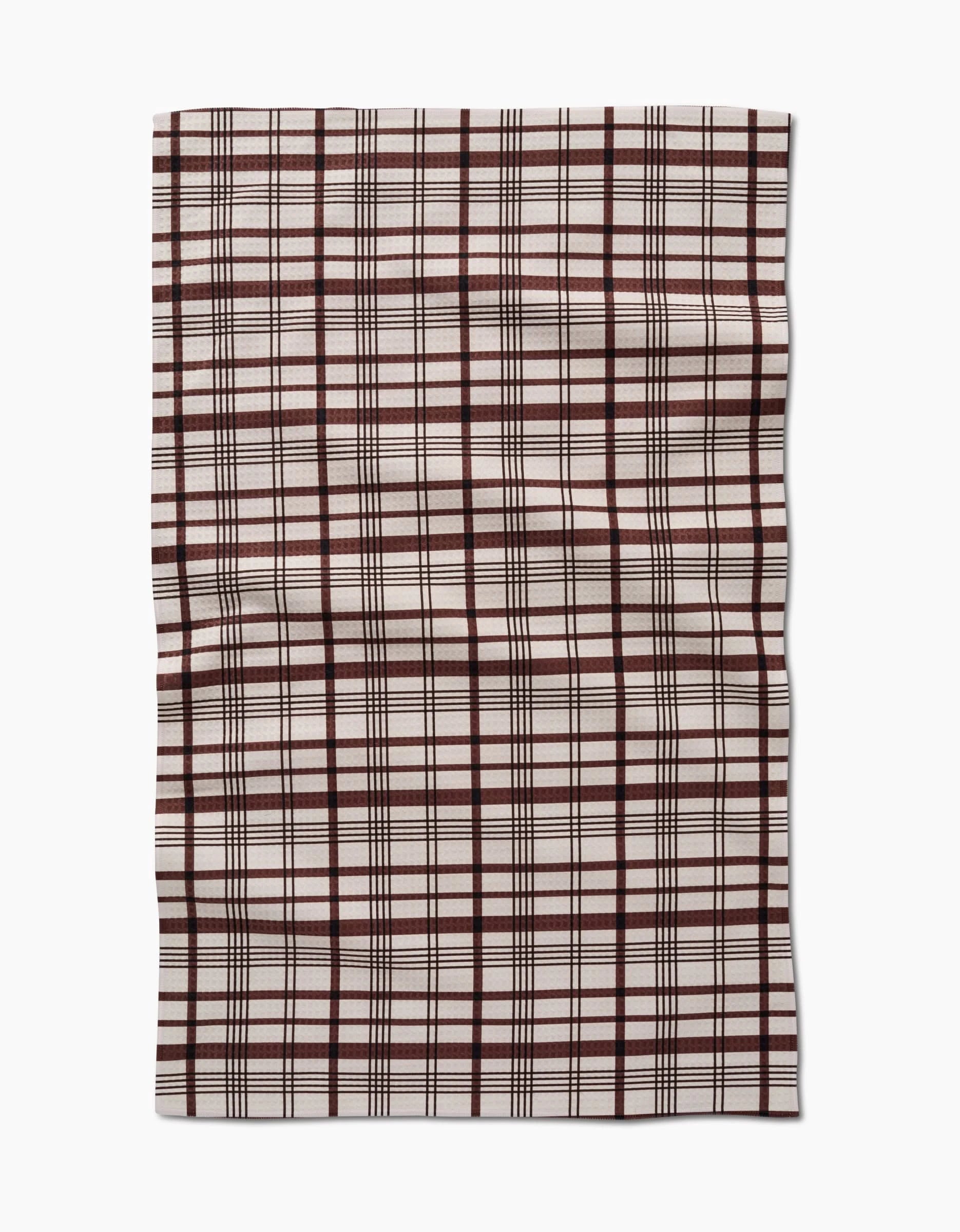 A rectangular Hufton Studio Vintage Plaid Natural hand towel with intersecting black and dark red lines on a white background, slightly wrinkled on a white surface. Features quick-drying Geoweave technology.