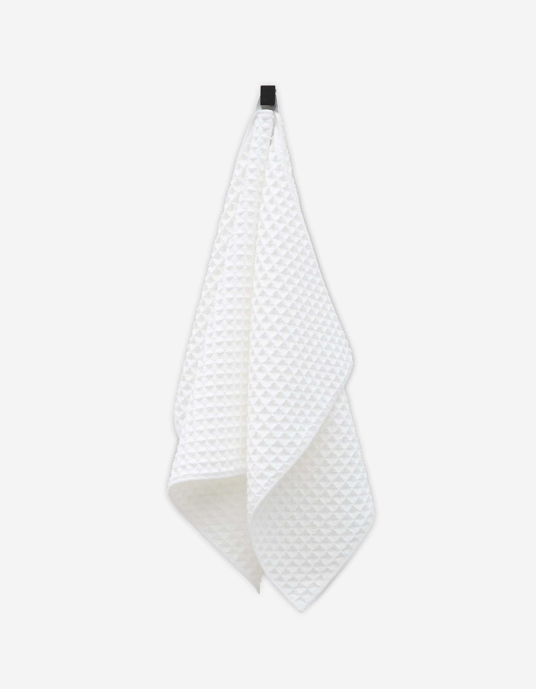 The GEOMETRY Cloud hand towel, featuring a white textured waffle pattern, hangs from a black hook against a plain white background, bringing subtle luxury to your space.