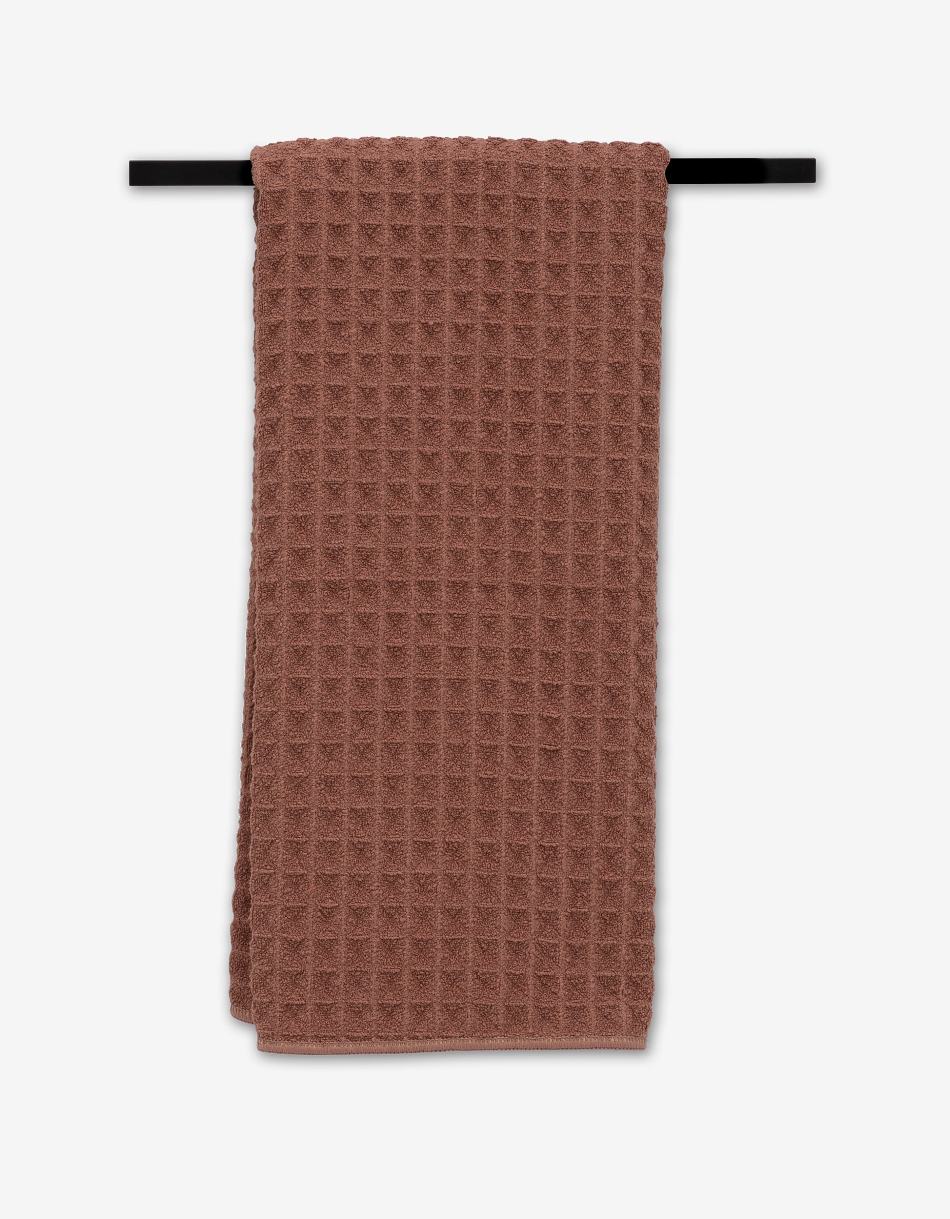 A Dusty Rose GEOMETRY hand towel hangs neatly folded over a black towel bar against a white background.