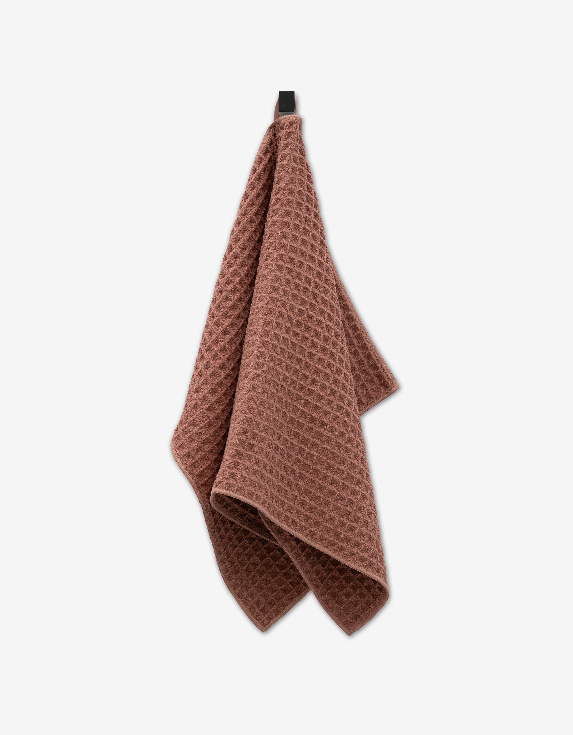 A dusty rose GEOMETRY Waffle Hand Towel with a waffle texture hangs from a black hook against a white background, offering ultra-absorbent luxury for your bathroom.