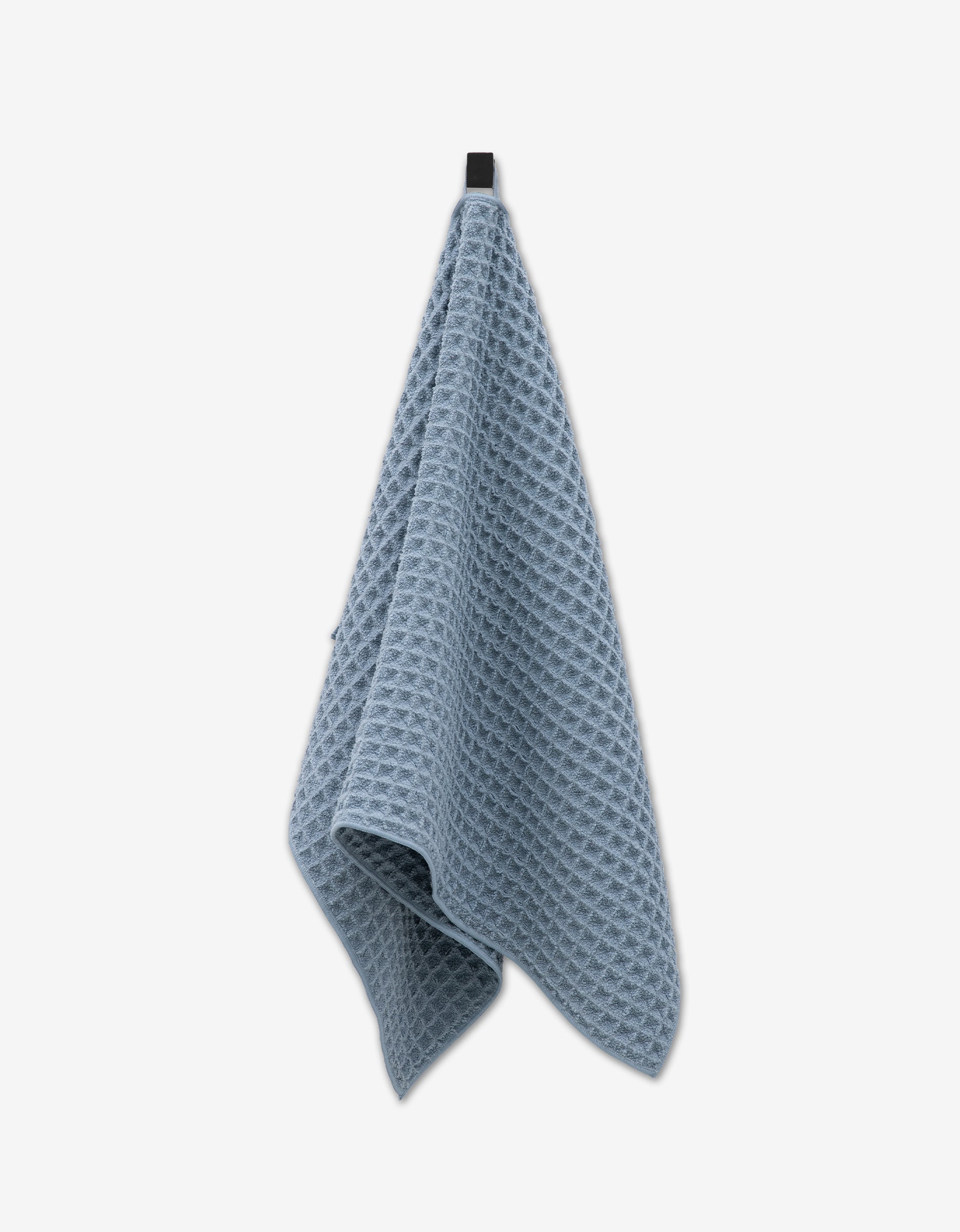 A GEOMETRY Sky hand towel in blue hangs from a black hook against a plain white background.