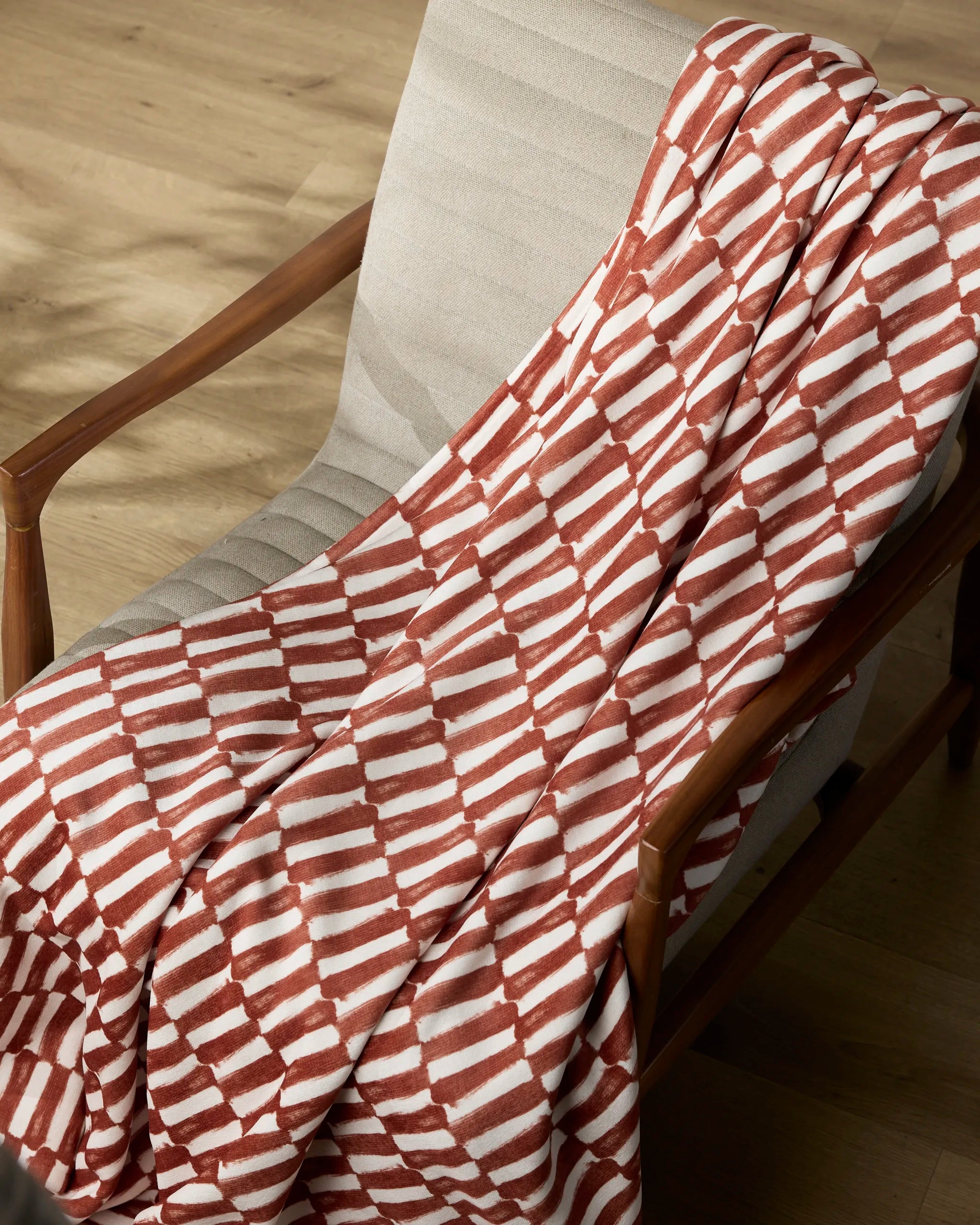 A cream-colored Clove upholstered chair by Geometry with wooden arms features a soft, silky Butter Blanket draped over it, set on a light wood floor.