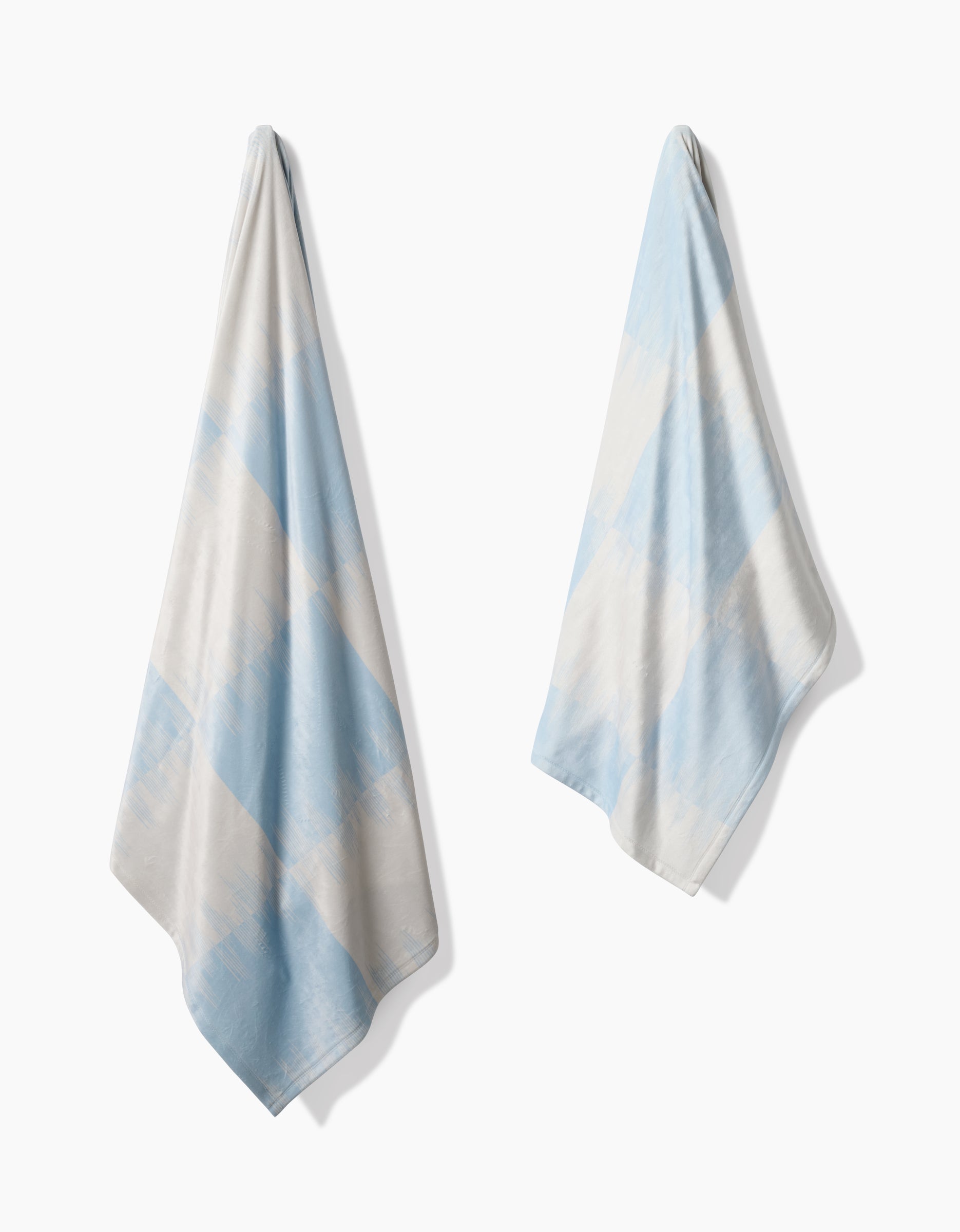 Two light blue and white Geometry Sweet Checks towels, made from recycled materials, feature a soft diagonal checkered pattern and hang separately against a white background.
