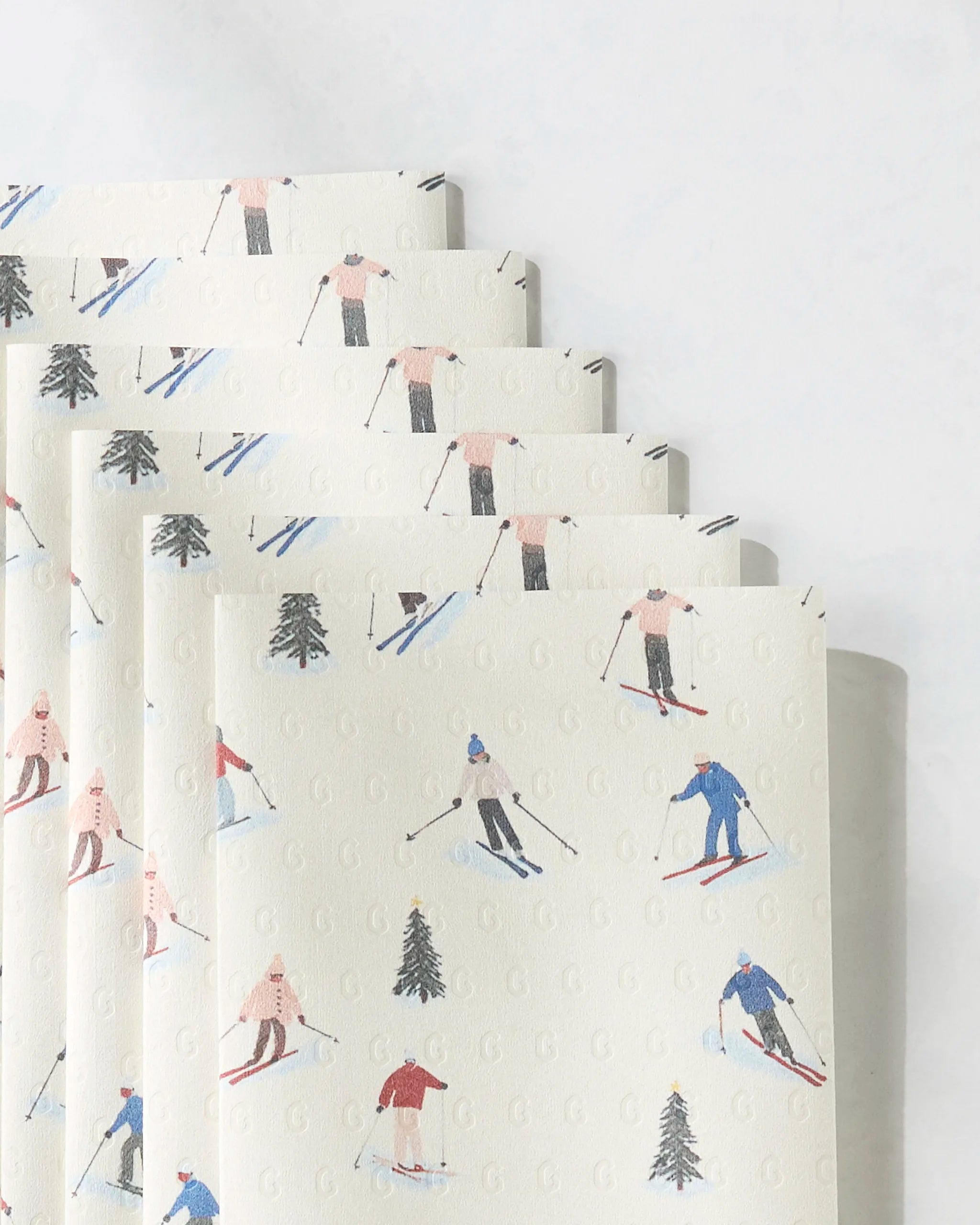Geometry’s Alpine Run paper towels are eco-friendly and feature a light background with small illustrated skiers in colorful outfits and pine trees.