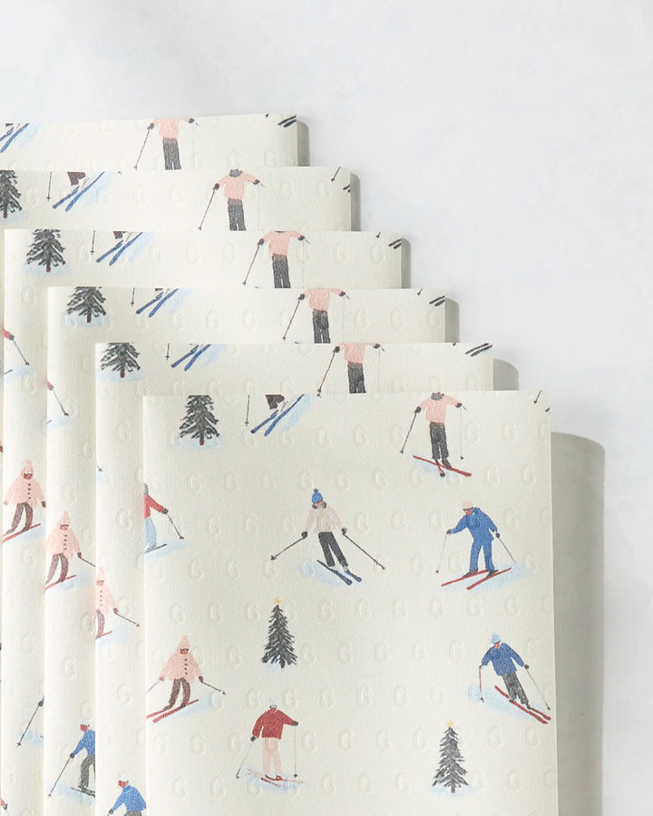 Geometry’s Alpine Run paper towels are eco-friendly and feature a light background with small illustrated skiers in colorful outfits and pine trees.
