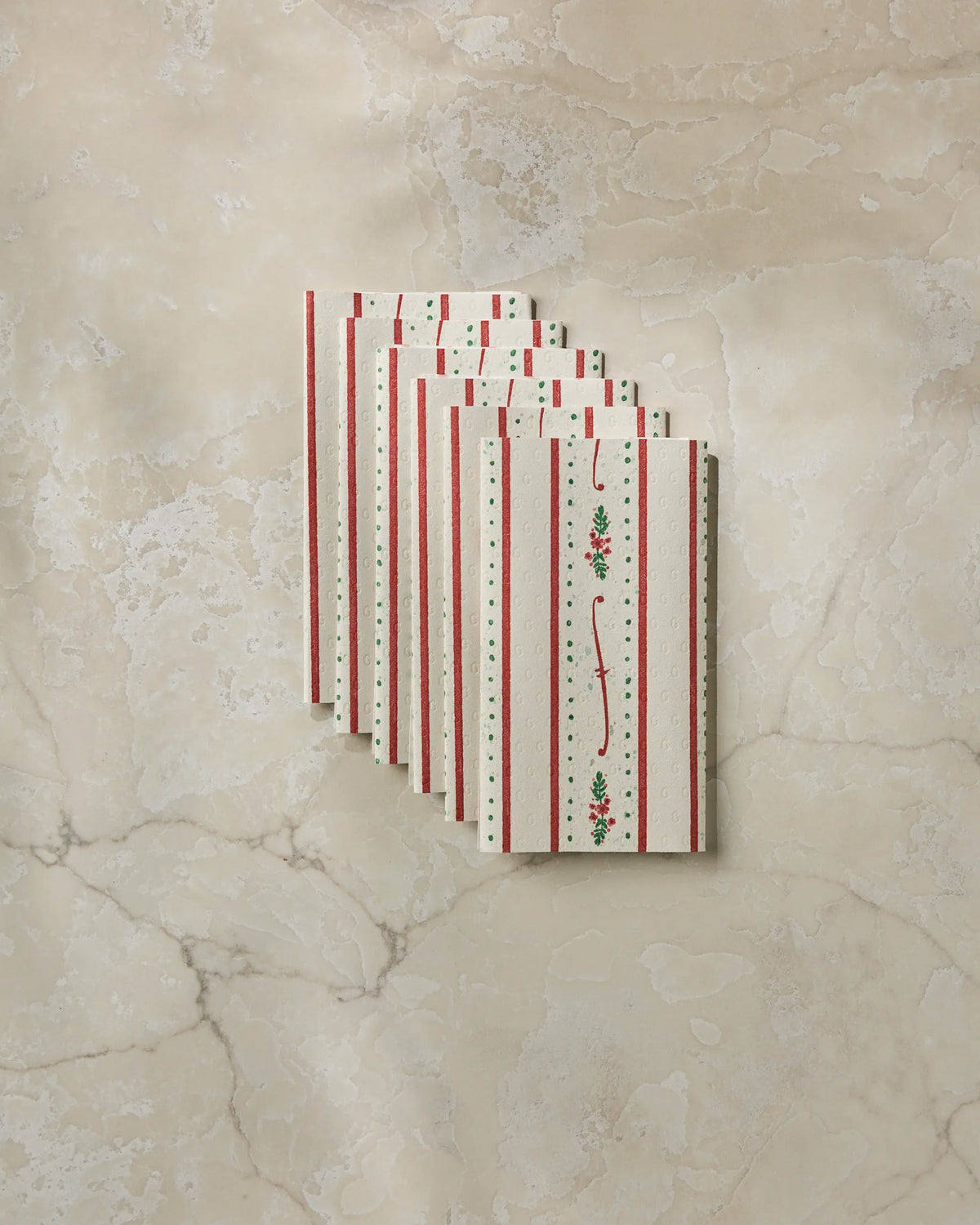 Eight “Alpine Trim” envelopes by Geometry, featuring red stripes and petite floral designs on a white background and crafted to resemble eco-friendly paper towels, are artfully fanned out on a light beige marbled surface.