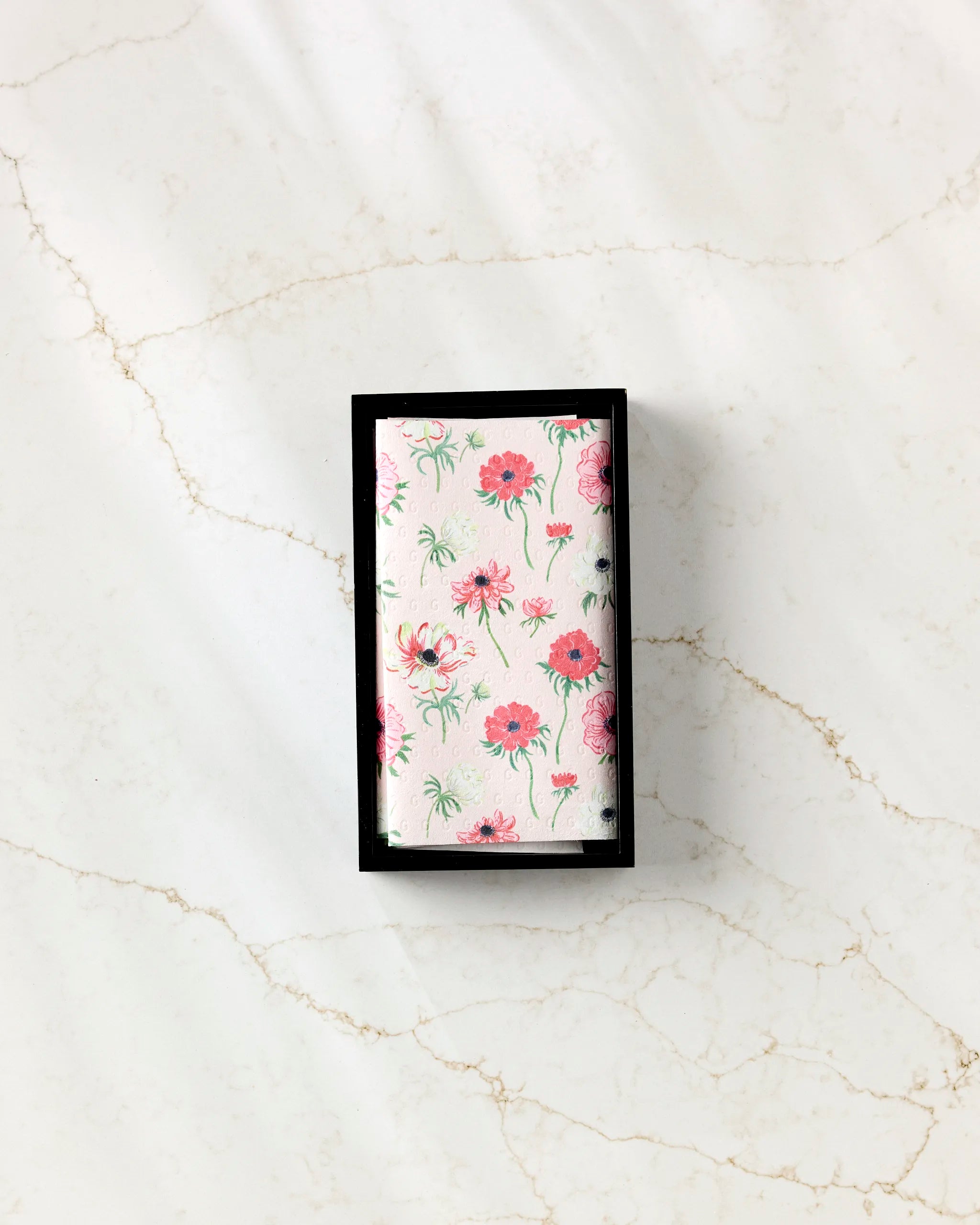 A rectangular box of Linda Fox Anemone Garden Flowers eco-friendly paper towels, featuring a floral cover with pink flowers and green stems, sits on a white marble surface with light brown veining.
