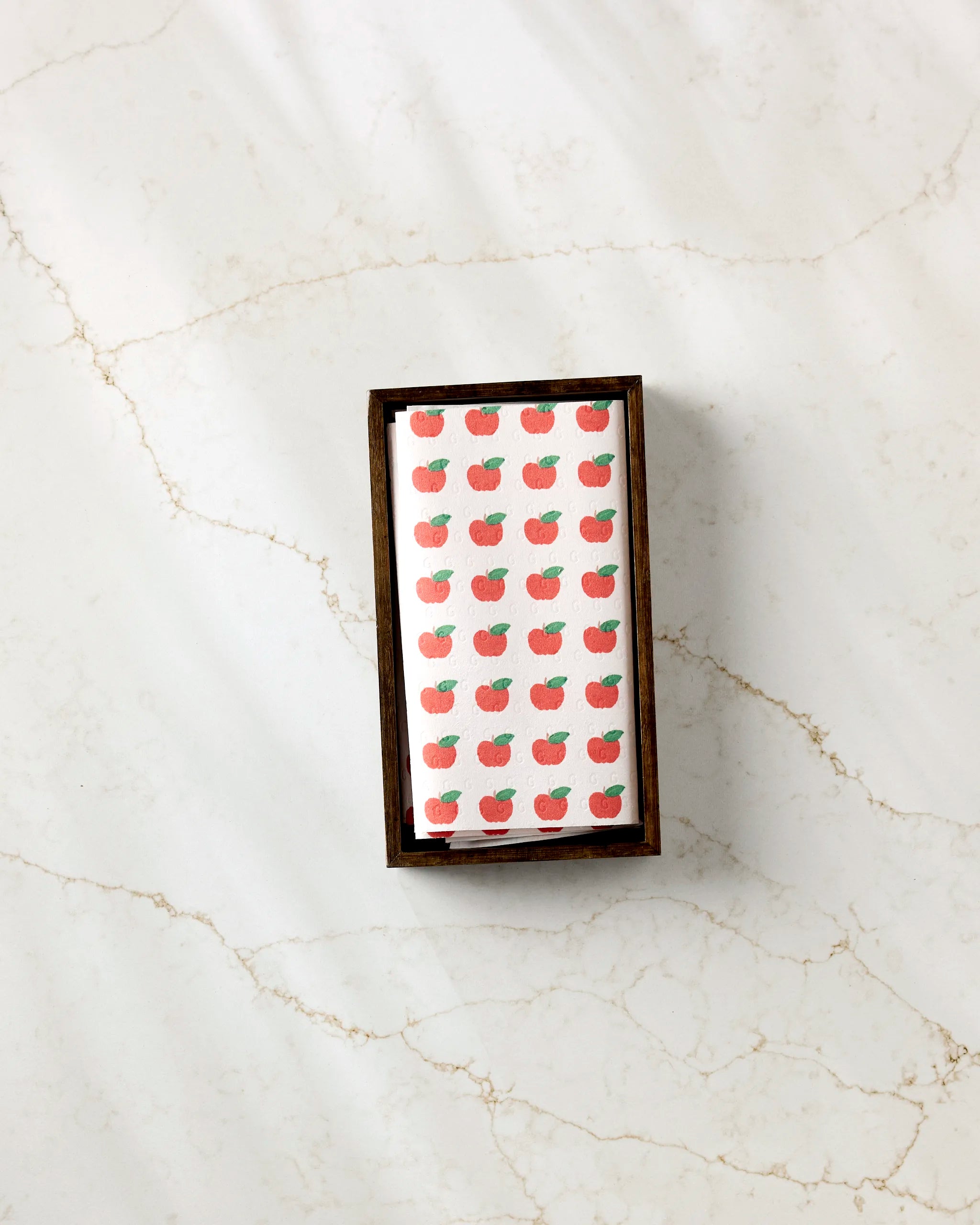 A small rectangular box labeled "Apple Grove" by Brittany Jepsen sits on a marble surface, holding cards adorned with a repeating red apple pattern, similar to those seen on eco-friendly reusable paper towels.