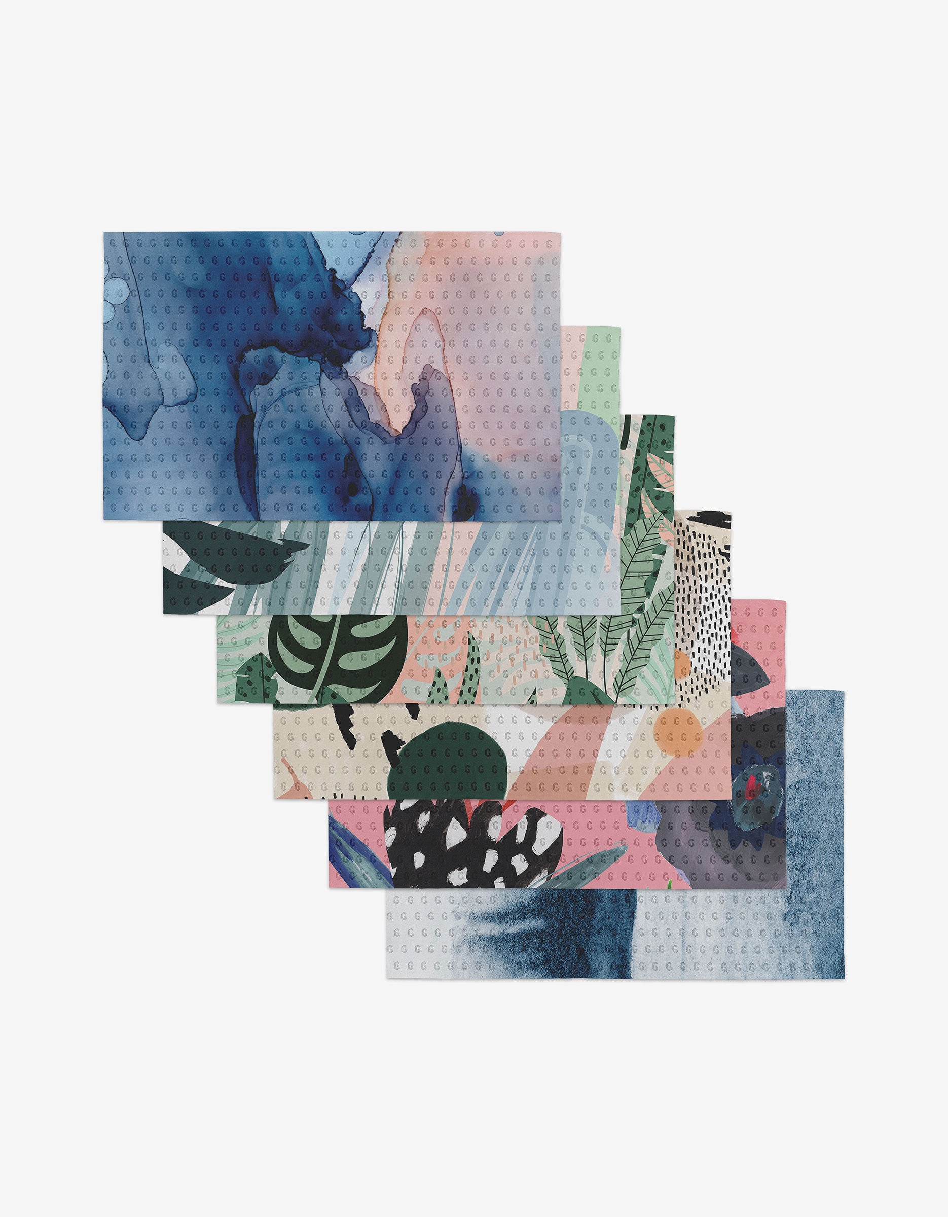 The GEOMETRY Artistic set includes six rectangular placemats, each with unique abstract and botanical watercolor designs in blue, green, pink, and beige. Made from post-consumer recycled materials with leafy motifs.