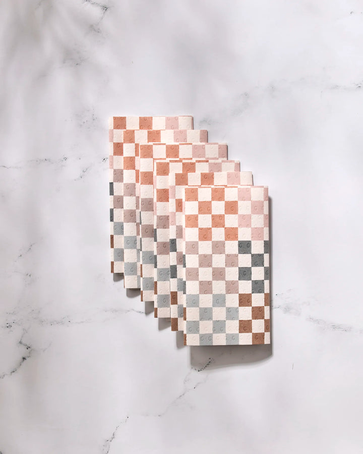 Five Autumn Checkers eco-friendly kitchen towels by GEOMETRY, featuring a beige, brown, and gray checkered pattern, are neatly stacked on a white marble surface.