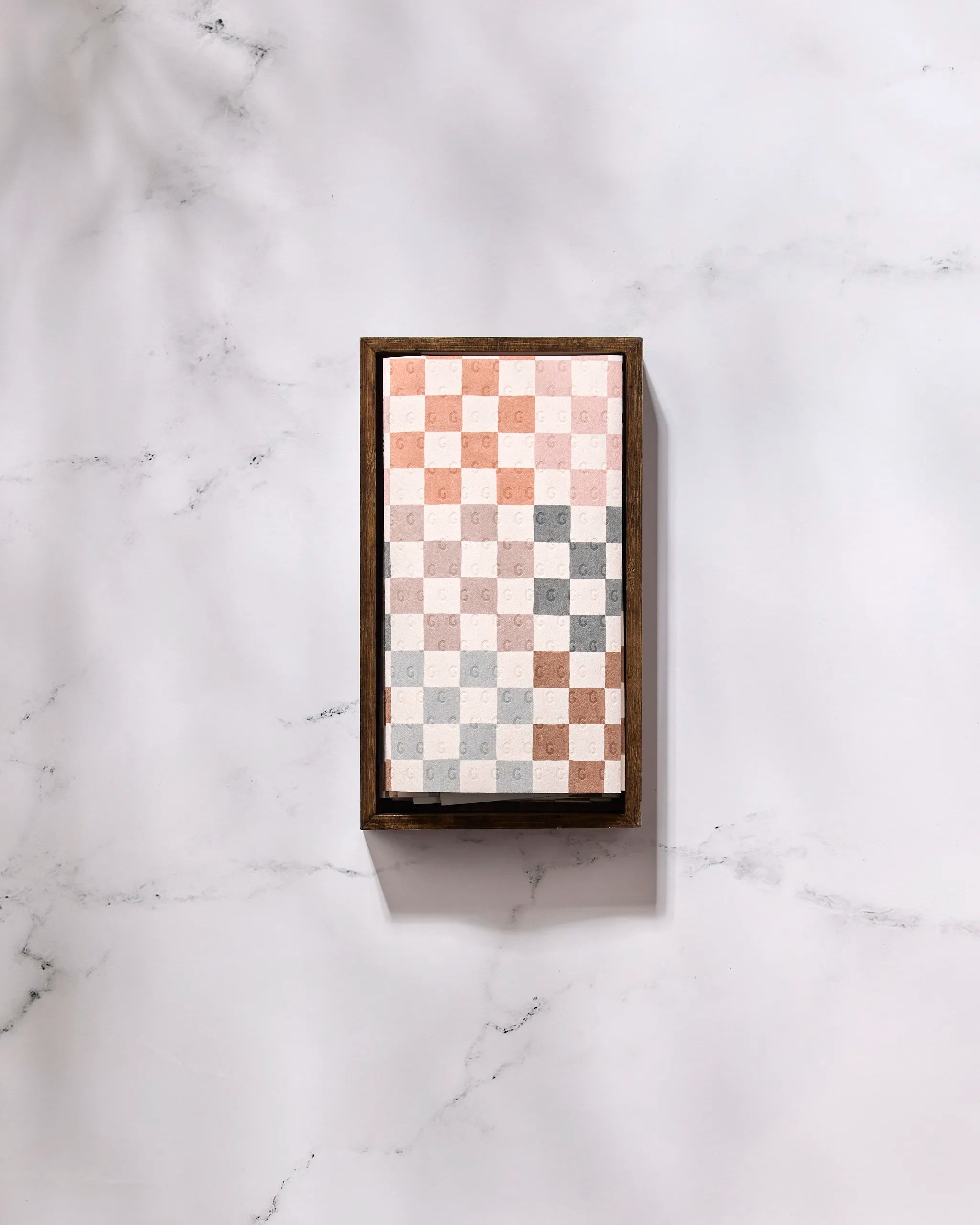 The GEOMETRY "Autumn Checkers" features a rectangular wooden tray of square chocolates in a white, light pink, light brown, and gray checkerboard—ideal for displaying treats sustainably with eco-friendly kitchen towels.