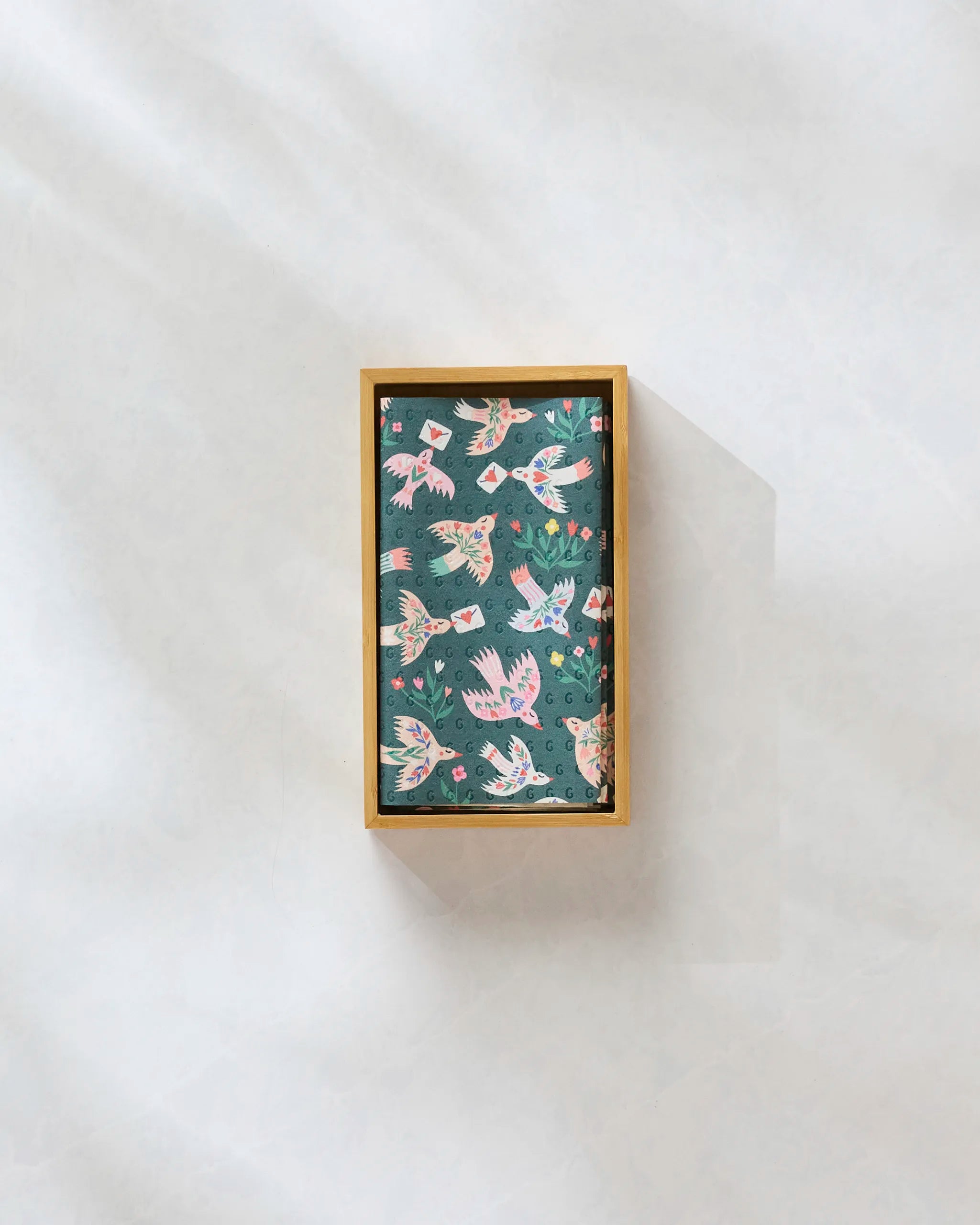 The Birdsong Post by Ceyda Alasar is a rectangular box with a lid, adorned with vibrant birds and flowers on a dark background—ideal for neatly storing reusable paper towels as an eco-friendly kitchen solution.