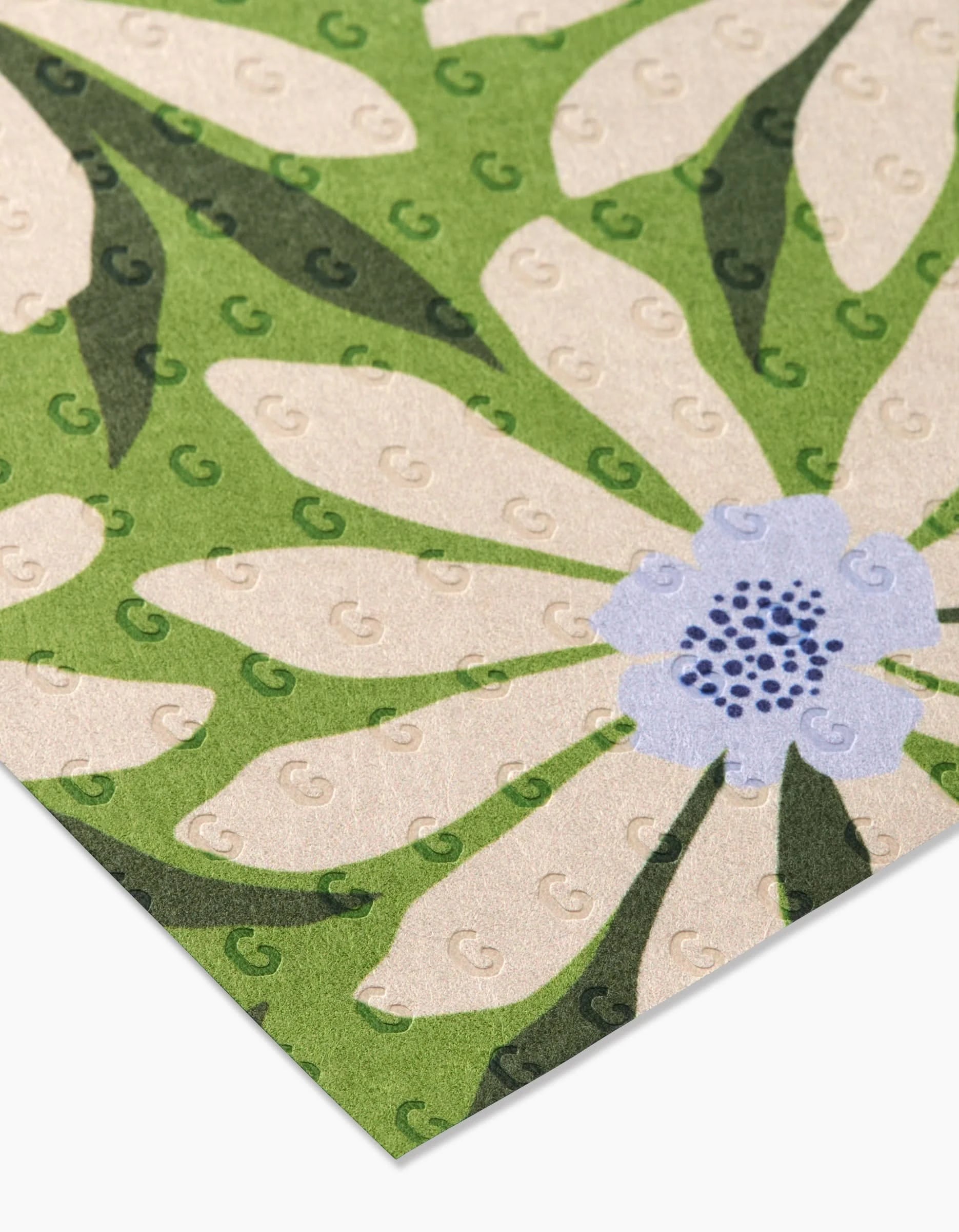 A close-up of GEOMETRYs Bliss and Bloom mat, featuring a large white and light blue floral pattern on green. Its surface has embossed G shapes, and its crafted from eco-friendly post-consumer recycled materials.