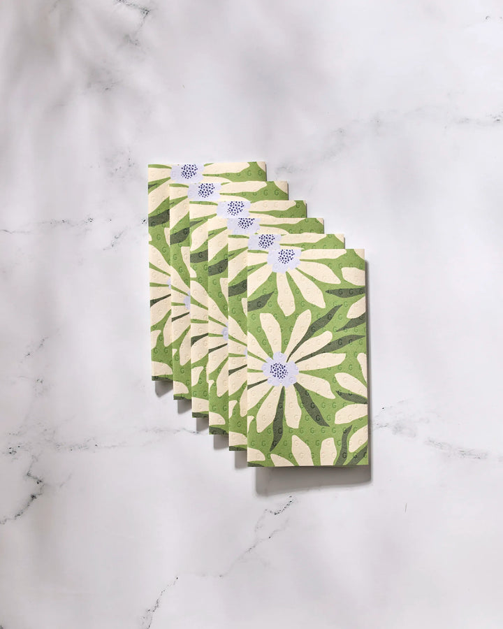 Six "Bliss and Bloom" greeting cards by GEOMETRY, featuring white daisies and green leaves, are arranged in a neat overlapping row on a marble surface. Crafted from eco-friendly paper towels for a sustainable touch.
