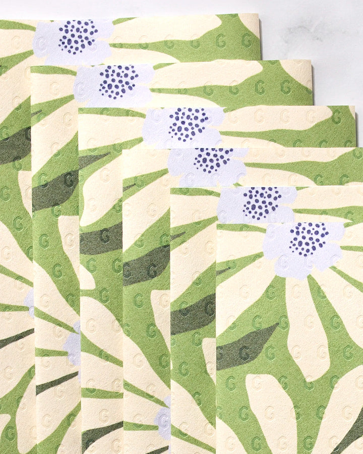 Five eco-friendly GEOMETRY Bliss and Bloom paper towels display a green and cream floral pattern with purple-centered flowers, arranged fanned-out and overlapping against a light background.