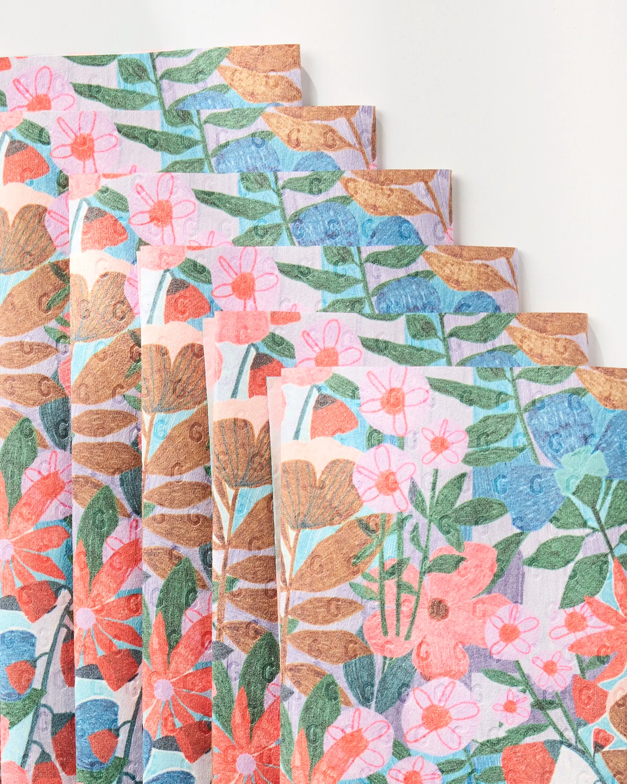 Bloom Entangled by Lisa Nelson: five stacked eco-friendly paper napkins with a vibrant floral design featuring red, pink, orange, and blue flowers plus green leaves on a light background.