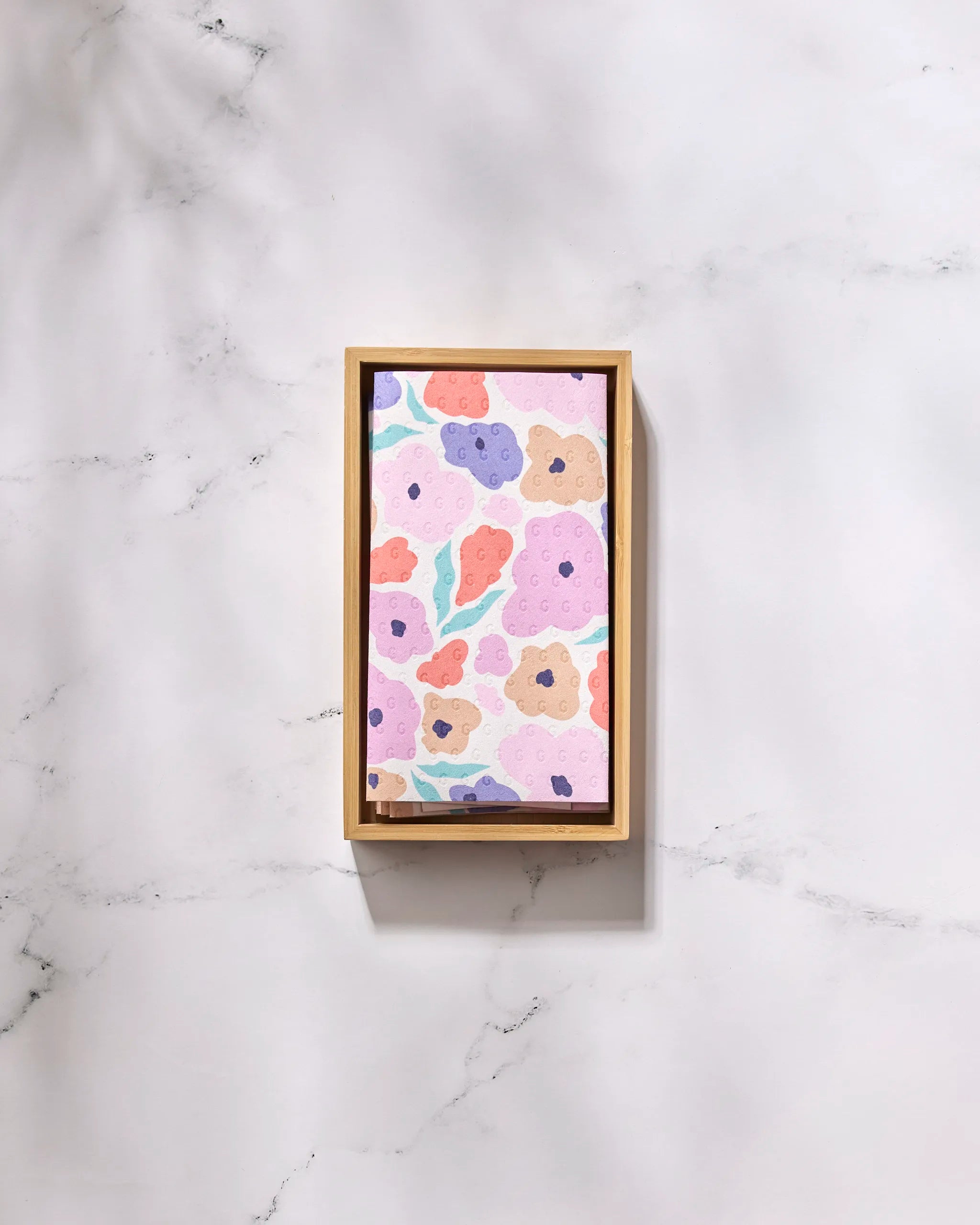 A rectangular tray with wooden edges and a pastel floral design holds eco-friendly Not Paper Towels, featuring GEOMETRY’s Blossoming Love pattern of pink, purple, orange, and blue abstract flowers with green leaves.