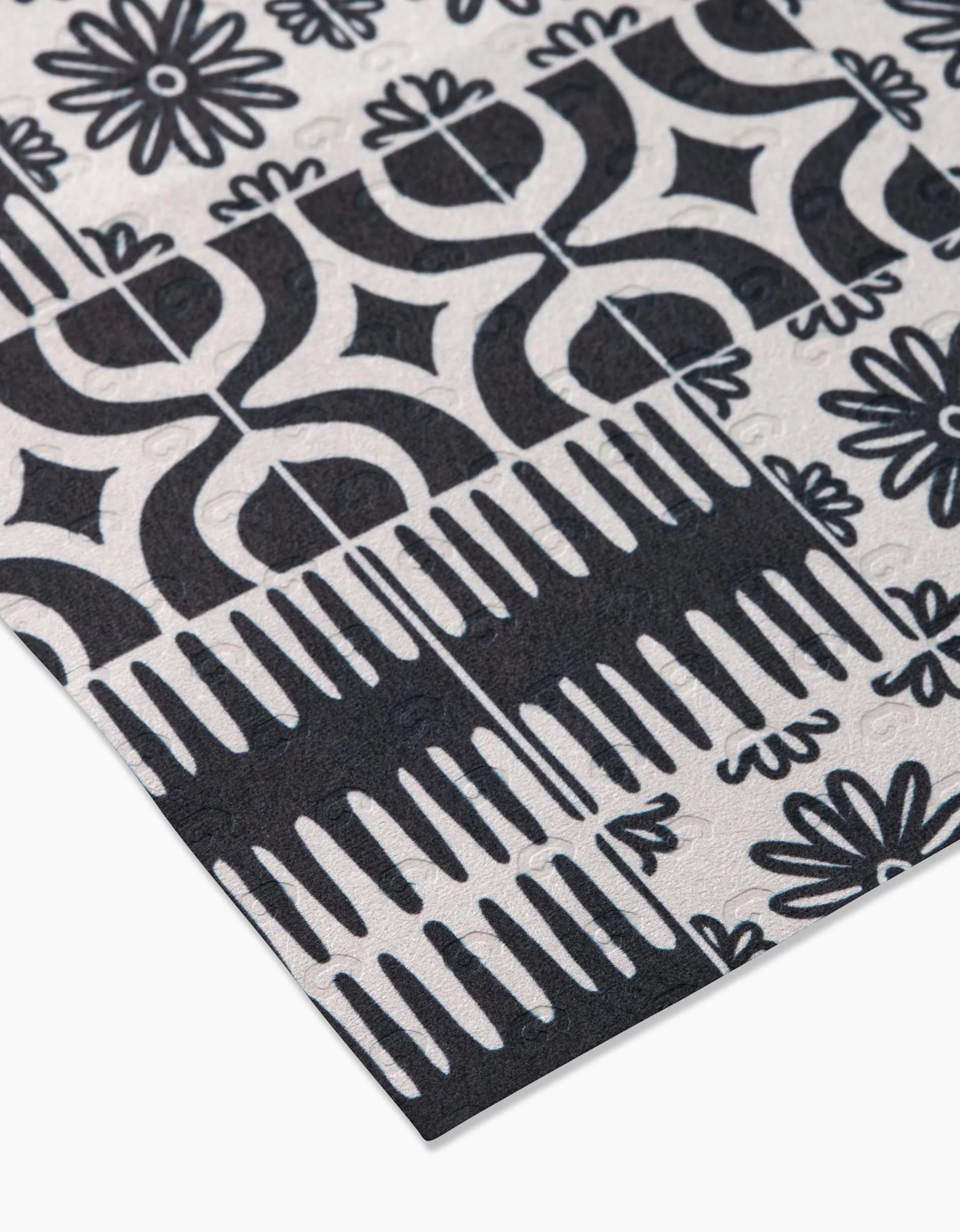 A close-up of GEOMETRY’s Bohemian Mosaic: a reusable patterned cloth with black and white geometric shapes, florals, and abstract lines in a tile-like repeat—an eco-friendly alternative to paper towels for your home.