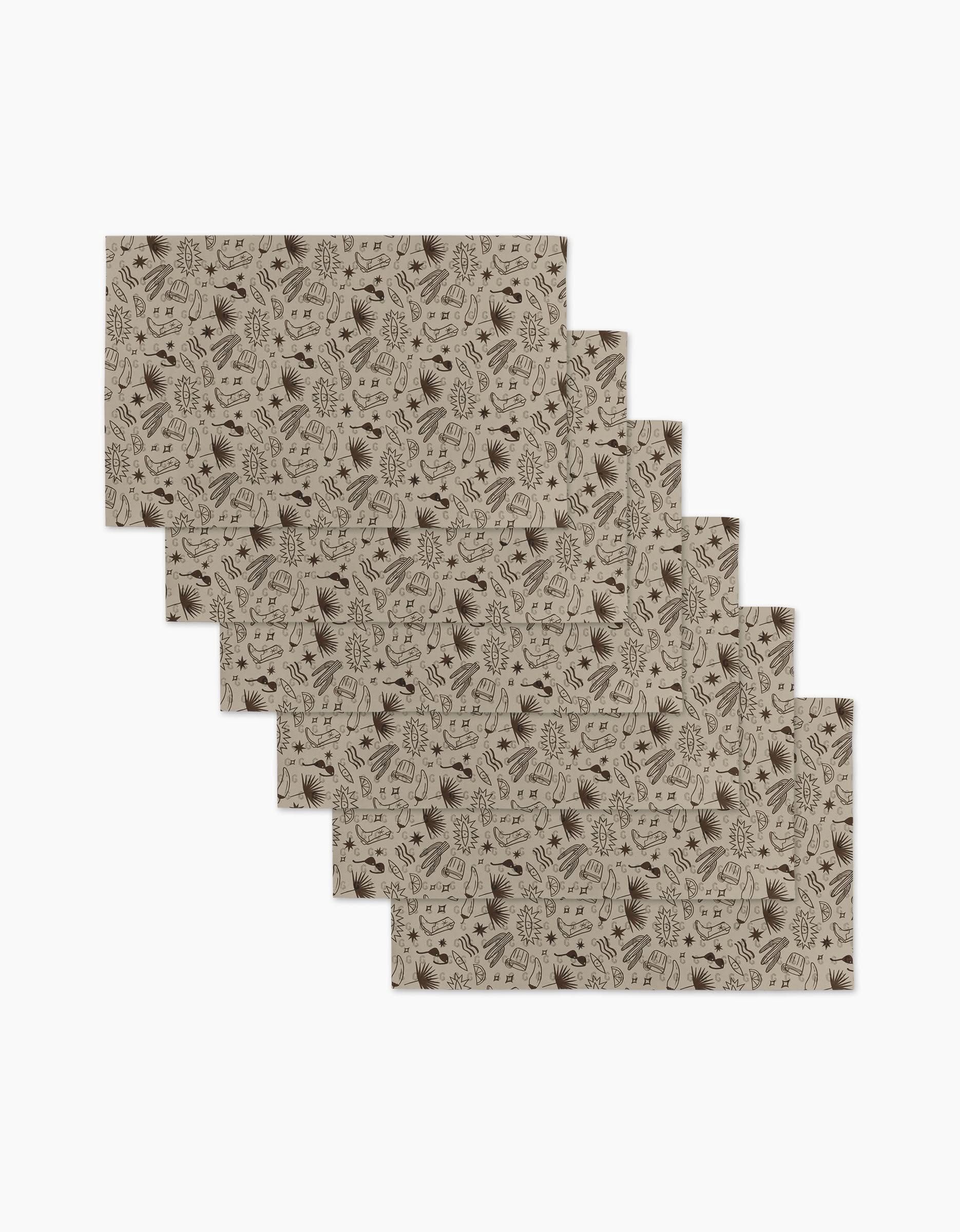 Six beige rectangular Bonfire Nights placemats by Geometry are stacked in a staggered pile. Reusable and eco-friendly, each features dark brown leaves and branches on white—sustainable, not paper towels.