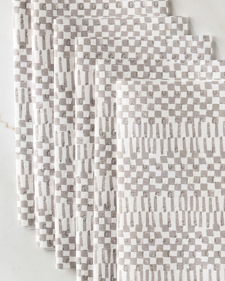 Four folded Chutes Coffee kitchen towels from Studio Jeannot, featuring an eco-friendly geometric beige and white checkered pattern, fanned out on a light surface.