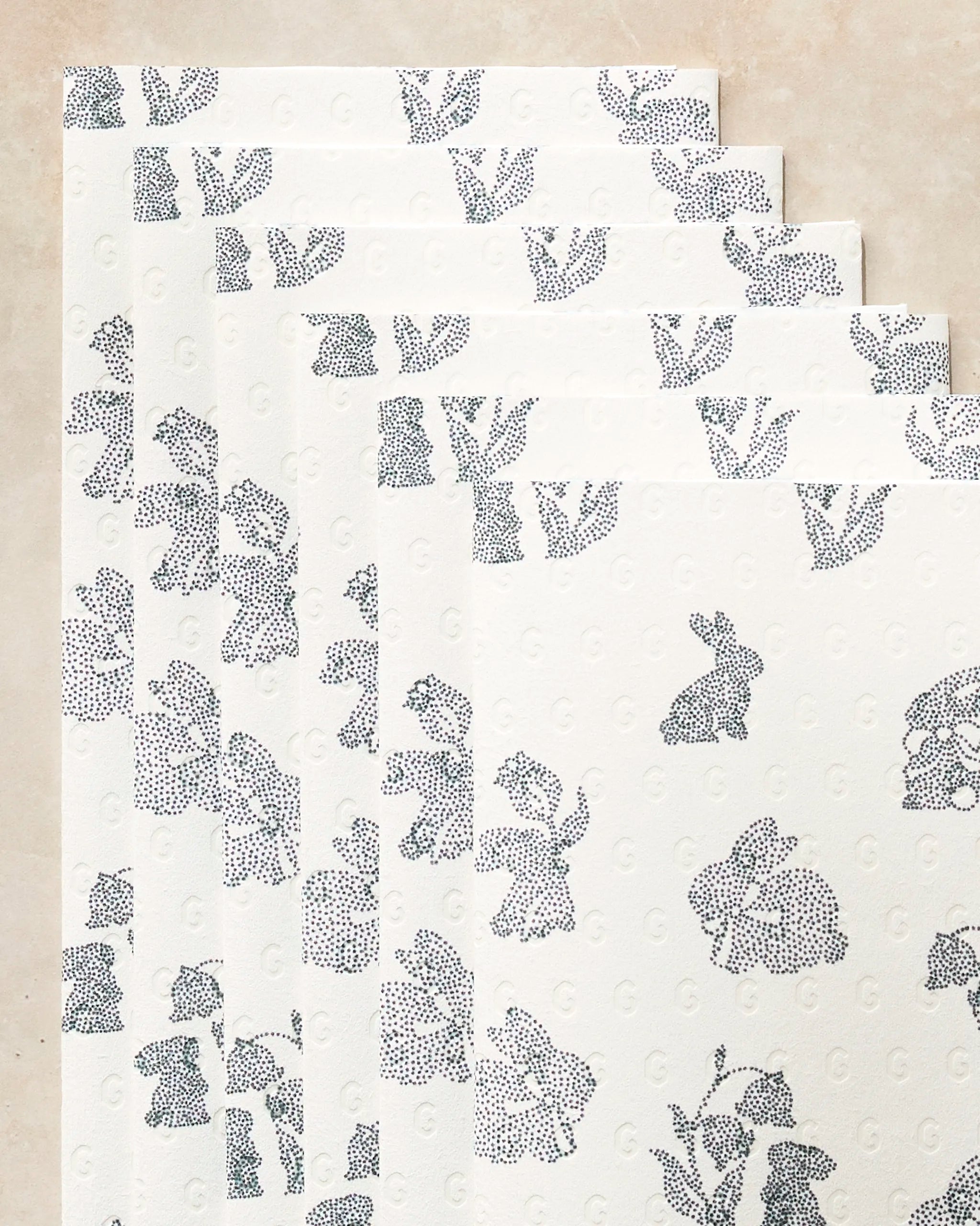 Geometry's Bunny Dots eco-friendly paper towels are arranged in a fan shape, each featuring a light background with a repeating blue dotted pattern of small bunnies and flowers.