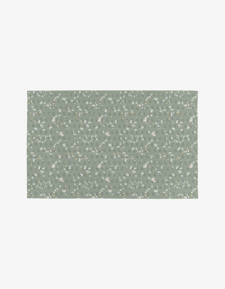 The Bunny Tea Time mat by Second Nature Studio is reusable and eco-friendly, with a muted green background featuring a delicate white and yellow floral pattern with green leaves evenly spread across its rectangular surface.