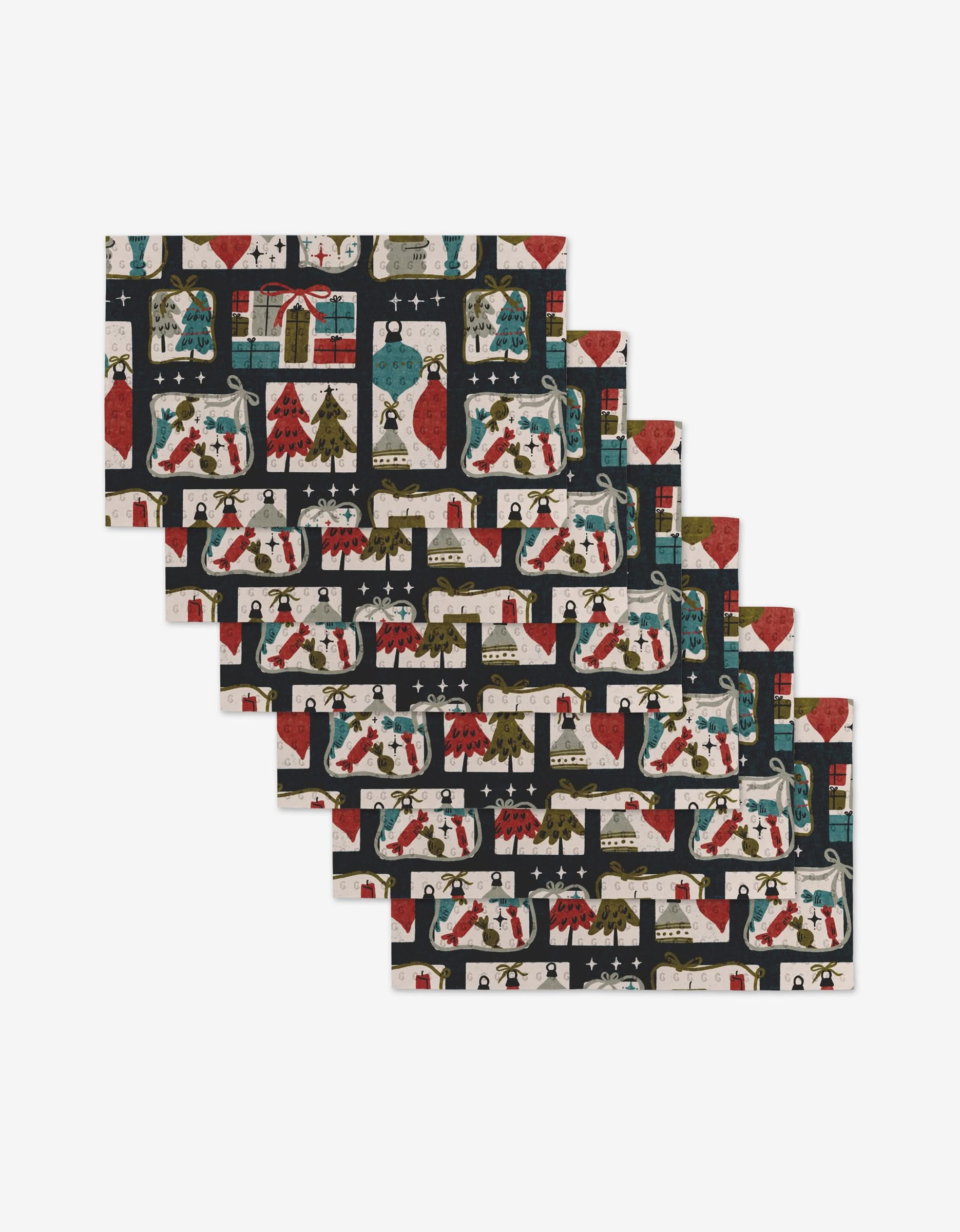 The Amy MacCready Cady Dark set includes six rectangular placemats made from eco-friendly recycled materials, decorated with Christmas stockings, trees, wreaths, and festive motifs in red, green, black, and white.