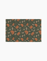 The Cali Sun mat by Amberleigh Adoff features orange rabbits, beige leaves, and dots on a dark green background for an eco-friendly touch inspired by reusable paper towels.