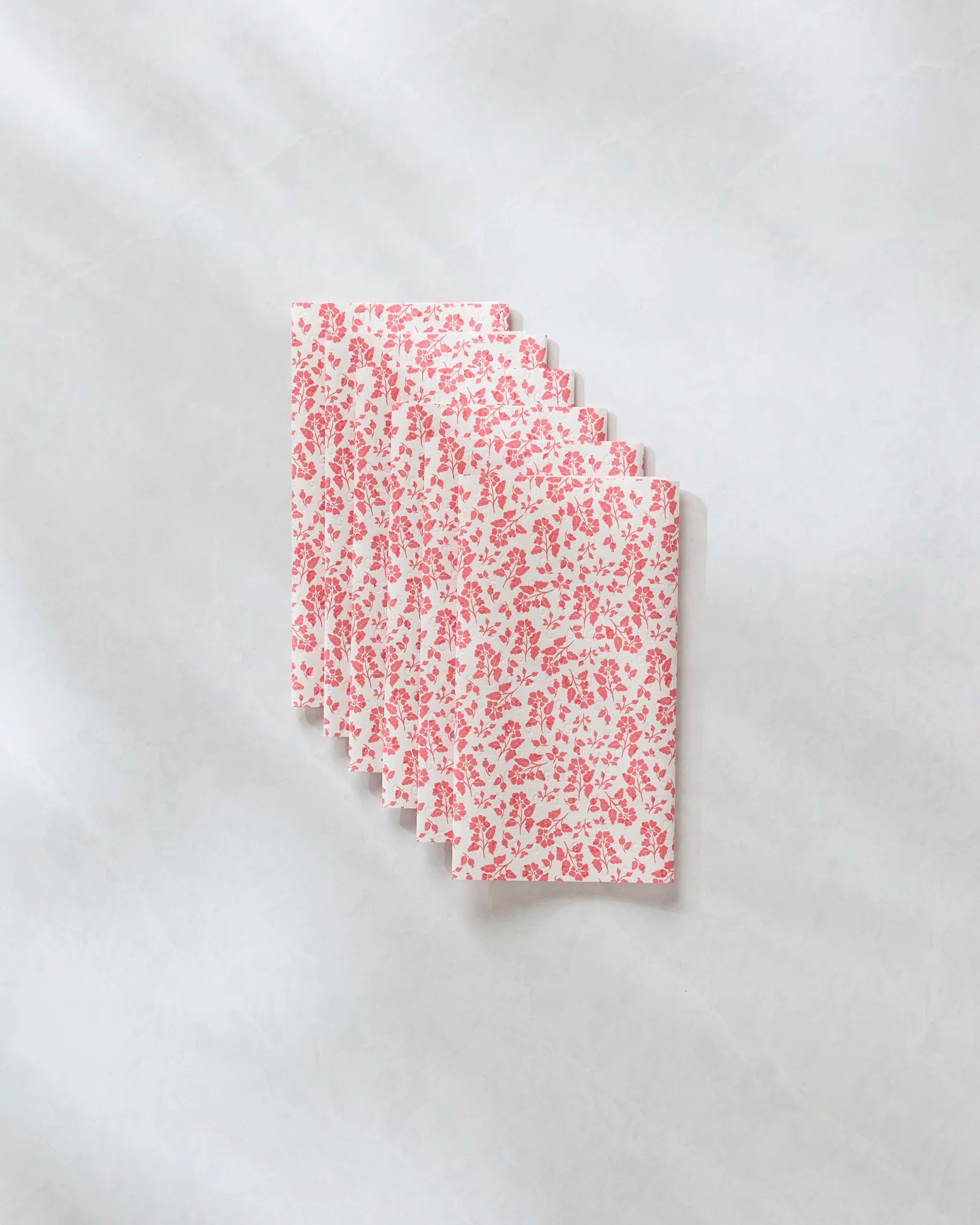 Five Carmine Garden cloth napkins by Danelys Sidron, featuring a red floral pattern on white, are fanned out on a marble-like surface—an eco-friendly kitchen towel alternative to paper towels.