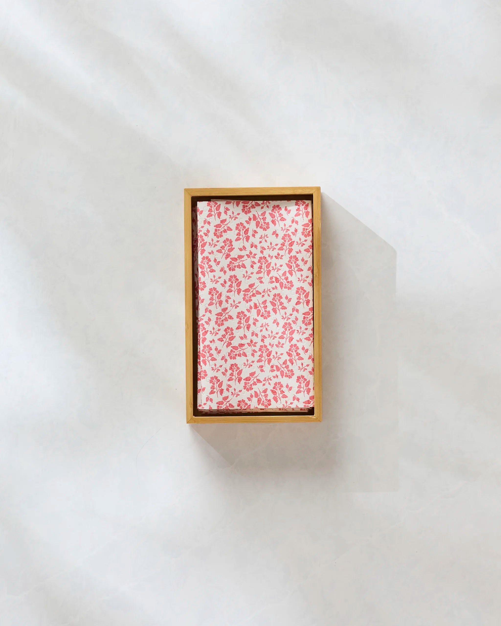 The Carmine Garden gold tray by Danelys Sidron, featuring a red and white floral pattern, sits centered on a light marble-like surface—perfect for displaying eco-friendly paper towels. Shadows fall to the right of the tray.