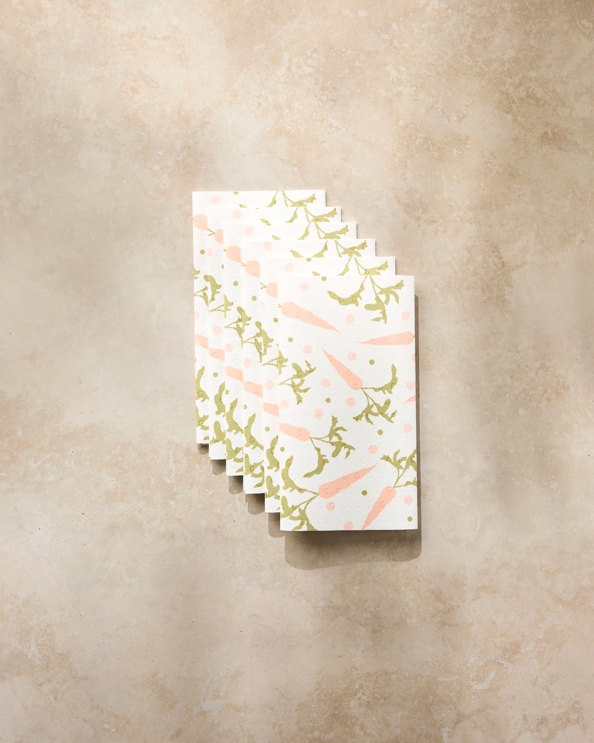 Six small, folded Geometry “Carrot Toss” cards with a pastel carrot and leaf pattern are fanned out on a light beige, textured surface.