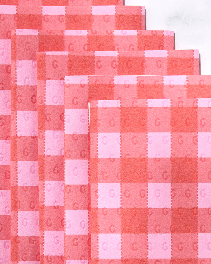 Four GEOMETRY Cherry Gingham reusable paper towels are stacked in a staggered arrangement. Each towel displays a pink and red gingham pattern with a small repeating letter G, set against a white marble background.