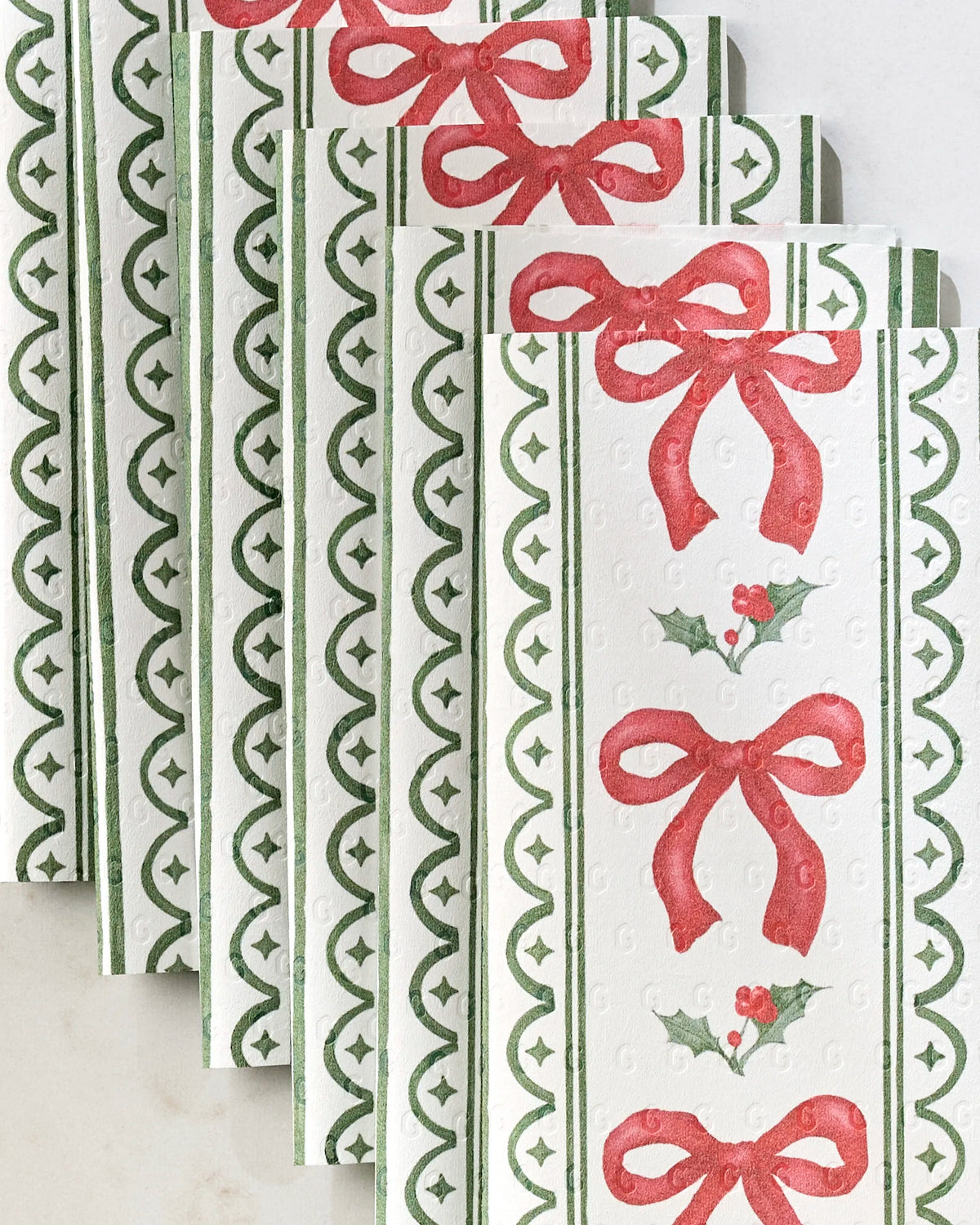 Aubrey Fairchild's Christmas Bow Stripe paper towels feature eco-friendly material with green borders, red bows, and holly leaf berry accents, neatly stacked on a light surface.