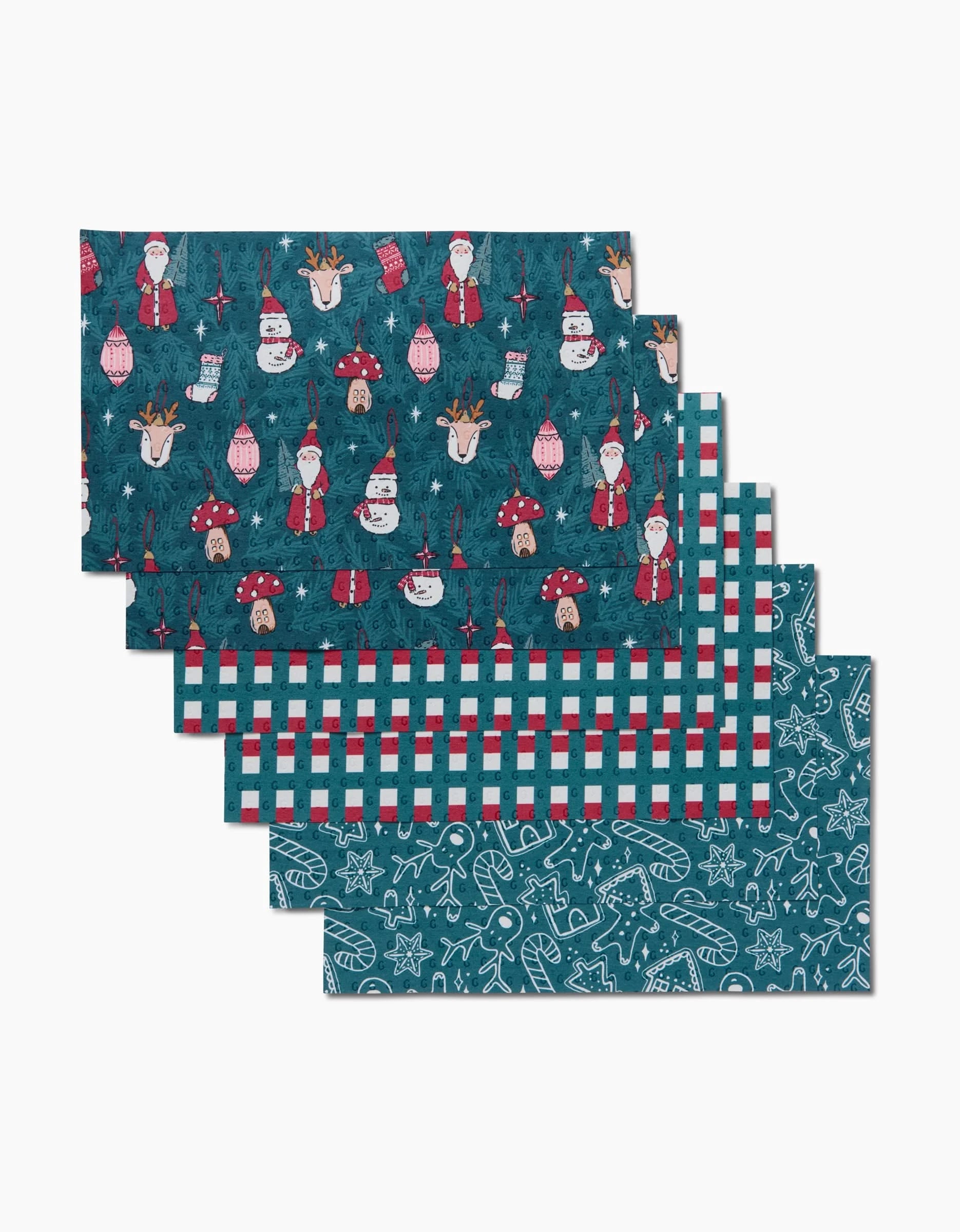 Six rectangular Christmas Traditions placemats by Hufton Studio: three with Santa, snowmen, reindeer, and ornaments; two in red, white, and blue plaid; one with Christmas cookie outlines on teal. Made from eco-friendly paper towels.