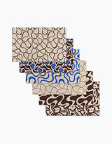 Five Coffee Reverie placemats by Gerdadzy, each with unique abstract and floral motifs in brown, beige, and blue, are fanned out. Made as an eco-friendly recycled paper towel alternative for sustainable style.