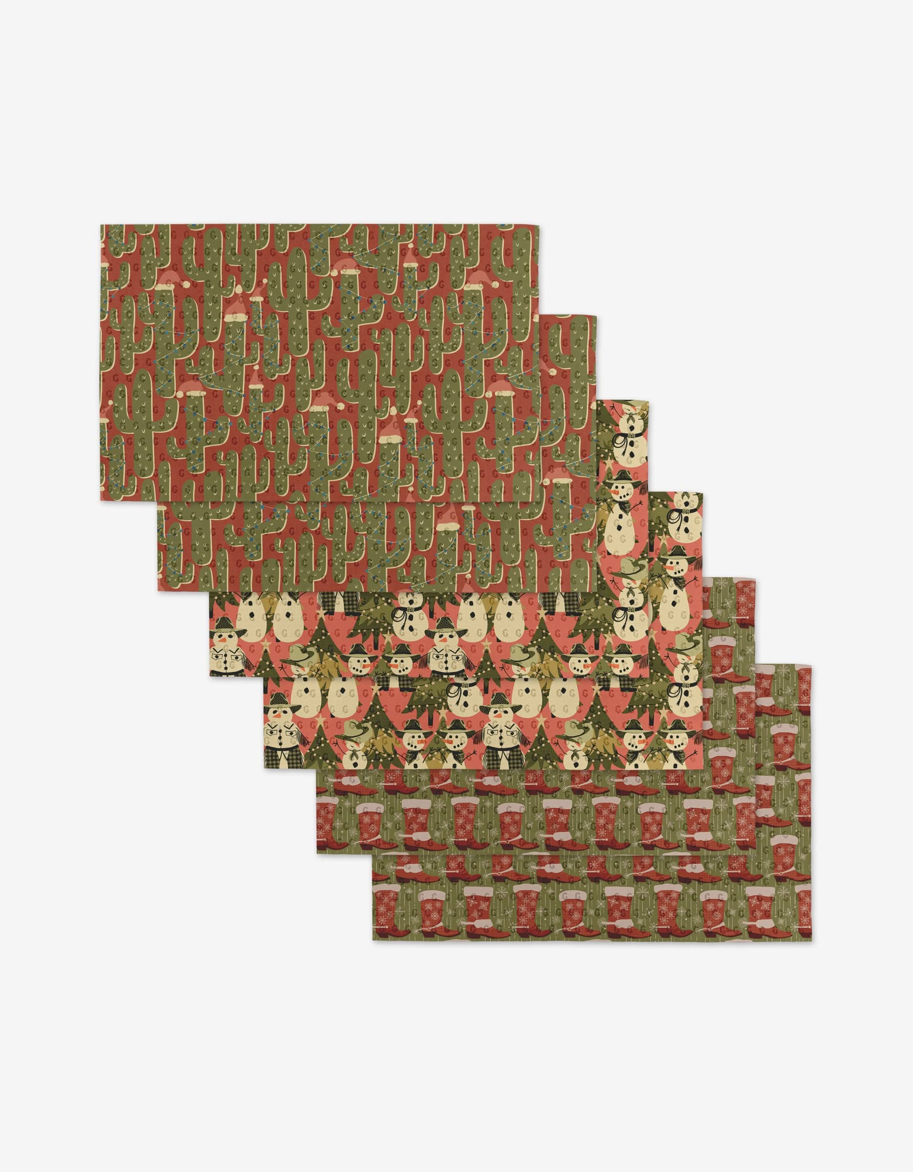 The Julianne Haness Cowboy Winter set features five reusable rectangular placemats with holiday cacti, snowmen, and reindeer in green, red, and beige, arranged in a staggered layout for festive, eco-friendly decor.