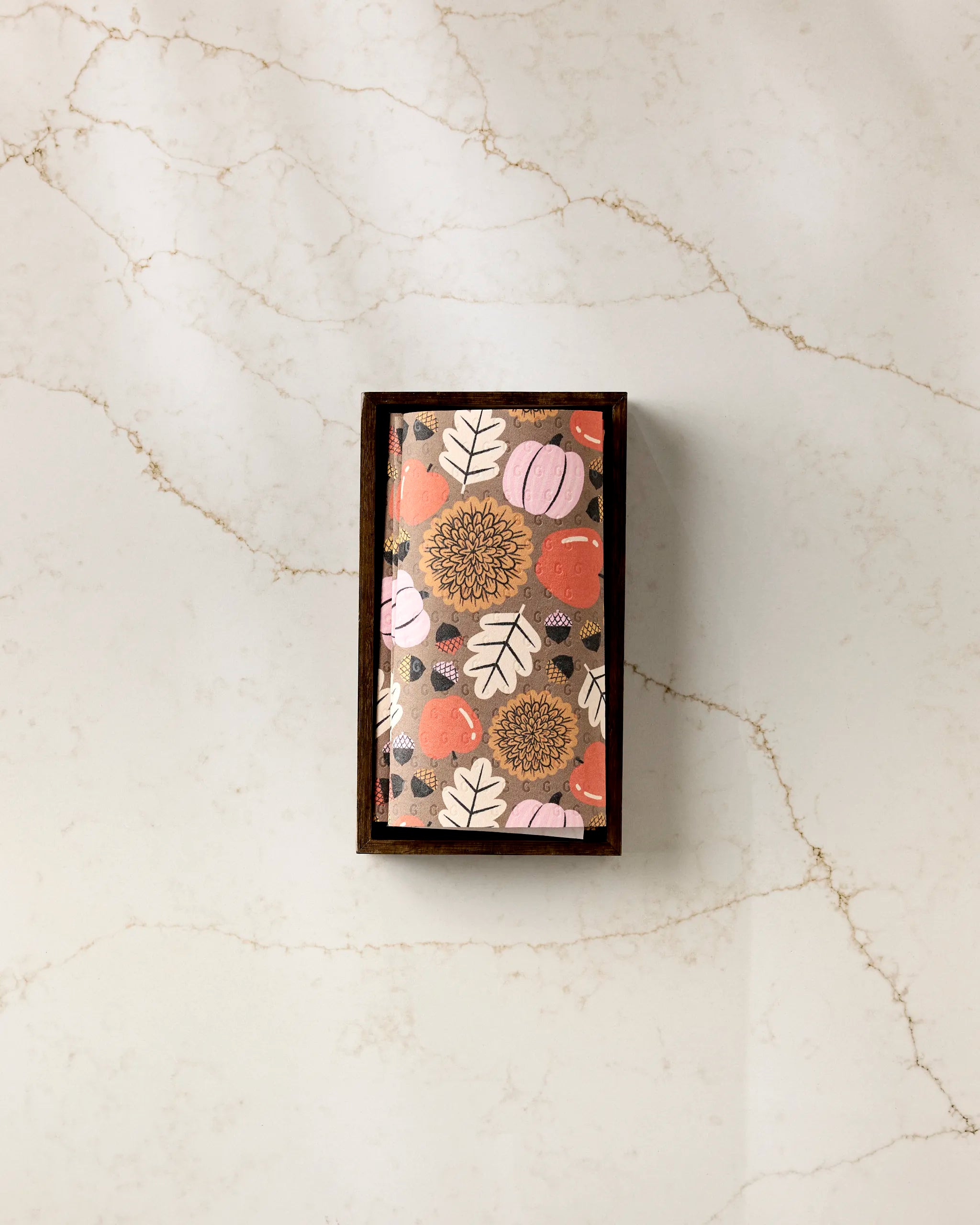 Crisp and Cozy by Megan Roy—a rectangular chocolate bar in a wooden box, wrapped in pink, orange, and beige floral-patterned eco-friendly paper towels, displayed on white marble with light brown veins.