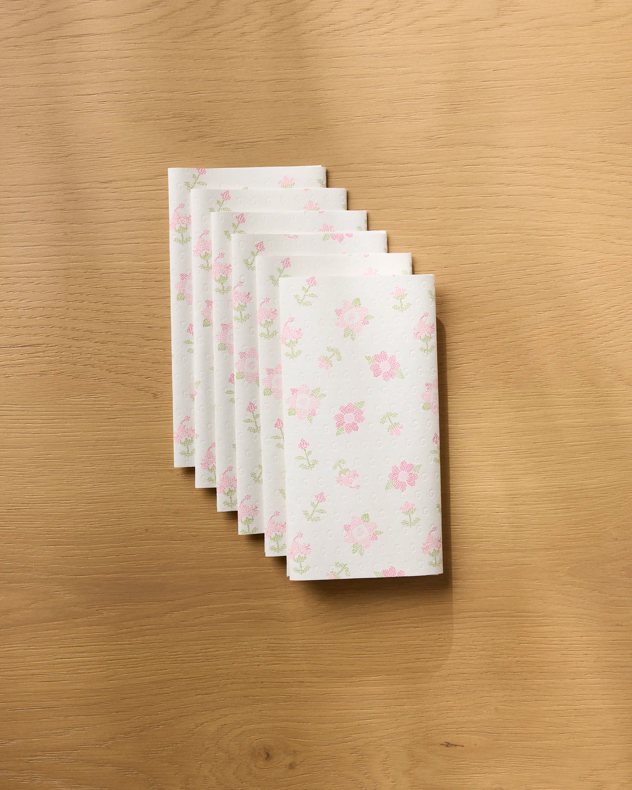 Six folded Geometry Cross Stitch Floral reusable paper towels are fanned out on a light wooden surface.