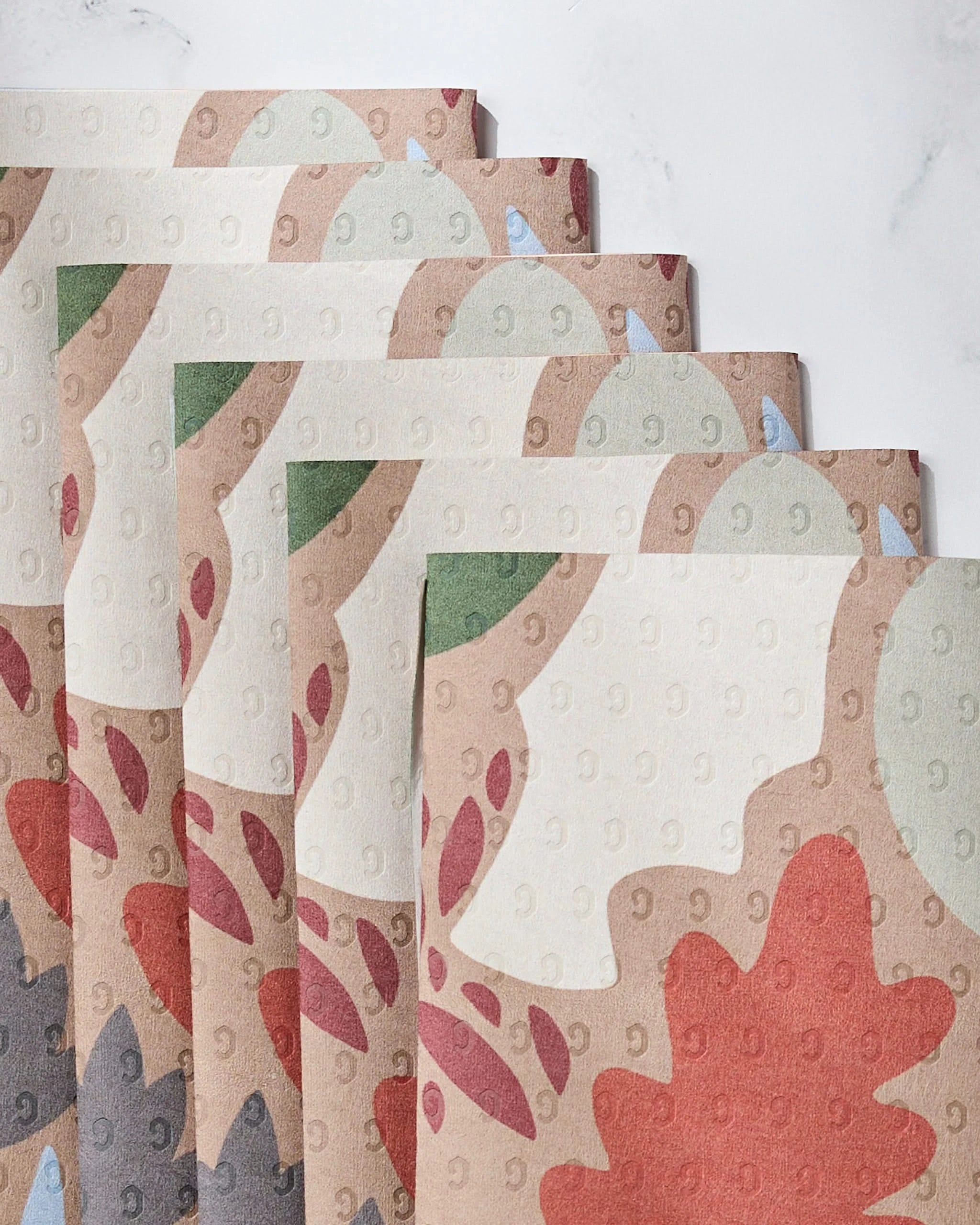 Five Cut Paper Leaves Mocha napkins by Geometry, stacked in a fan on white, feature a fall-inspired red, green, and brown leaf design and are made from post-consumer recycled materials for an eco-friendly option.