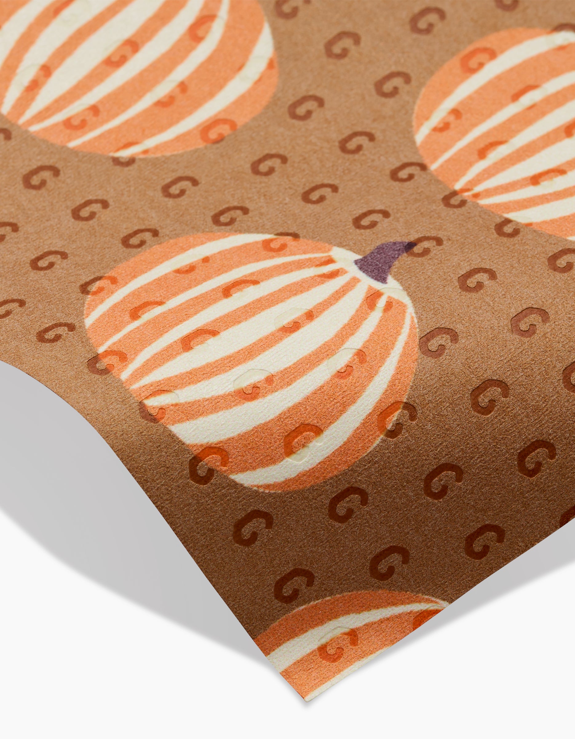 The Lizzie Clark Dancing Fall reusable paper towel is brown and eco-friendly, featuring an orange and white striped pumpkin pattern with subtle “G” shapes and a slightly curled corner.