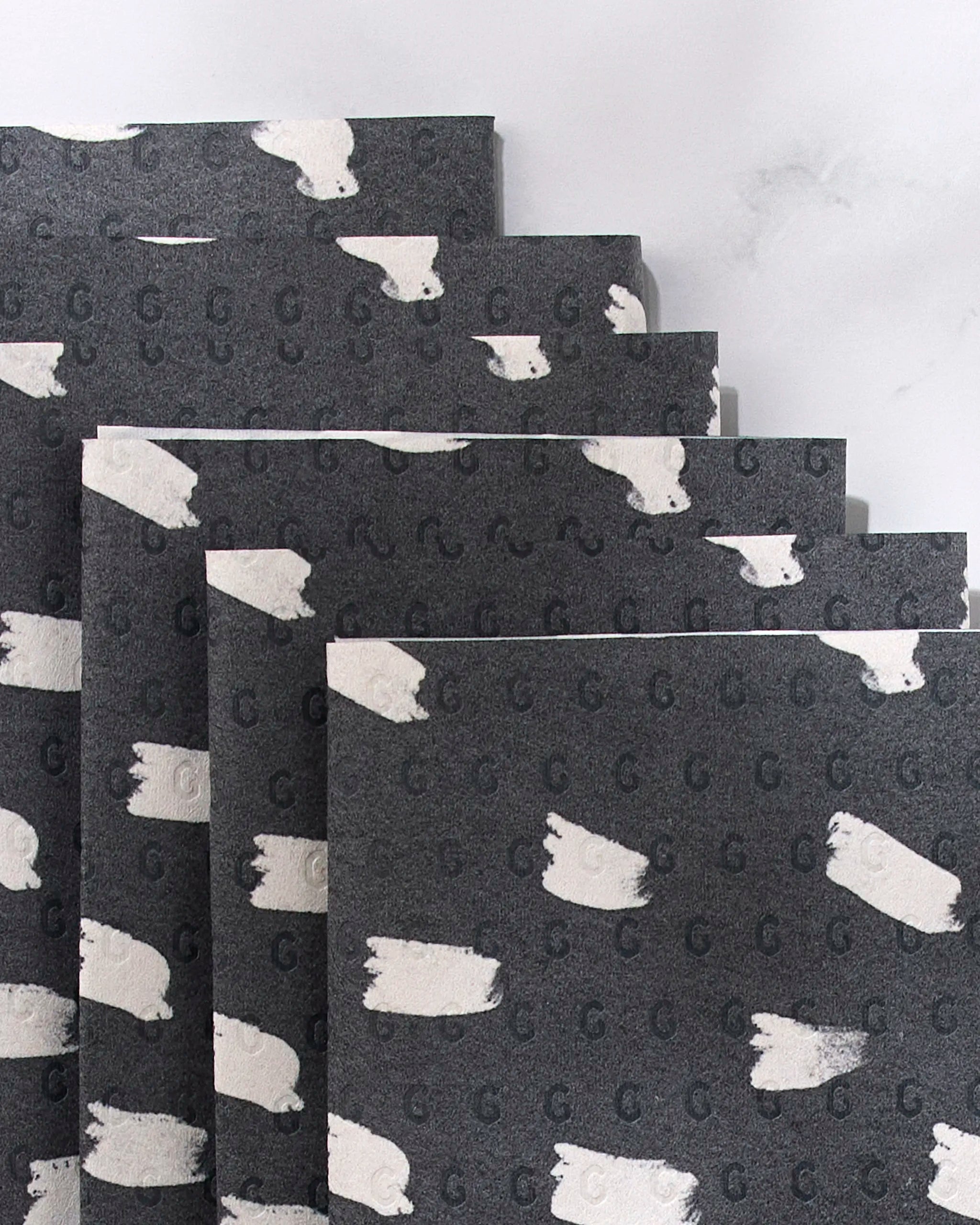 Dark Out by GEOMETRY: sheets of dark gray, post-consumer recycled paper featuring a pattern of small white polar bears and subtle letter Gs, stacked in a staggered formation on a light surface.