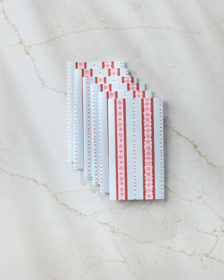 Geometry’s Dreaming of You envelopes, featuring blue and white heart and lace patterns, are fanned out on a marble surface next to Geometry’s eco-friendly paper towels for a charming, sustainable touch.