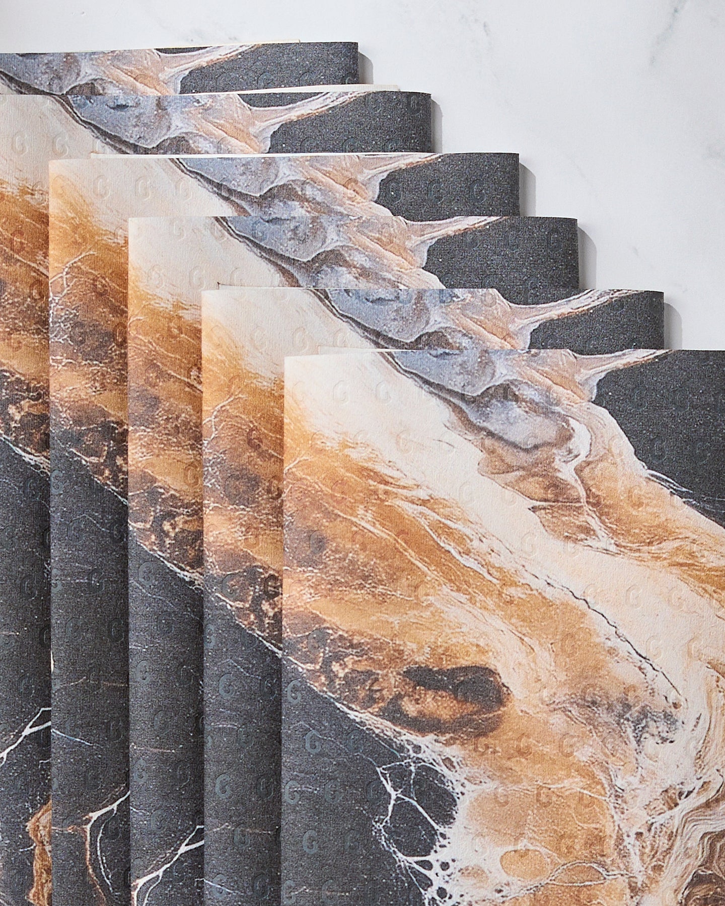 Geometry’s Emperador towels, featuring a marble-like pattern in brown, black, and white, are stacked in an overlapping arrangement on a light surface.