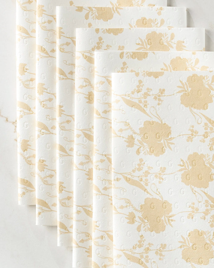 Six folded GEOMETRY Eternal reusable white and gold floral-patterned paper towels are neatly arranged in an overlapping row on a light marble surface.