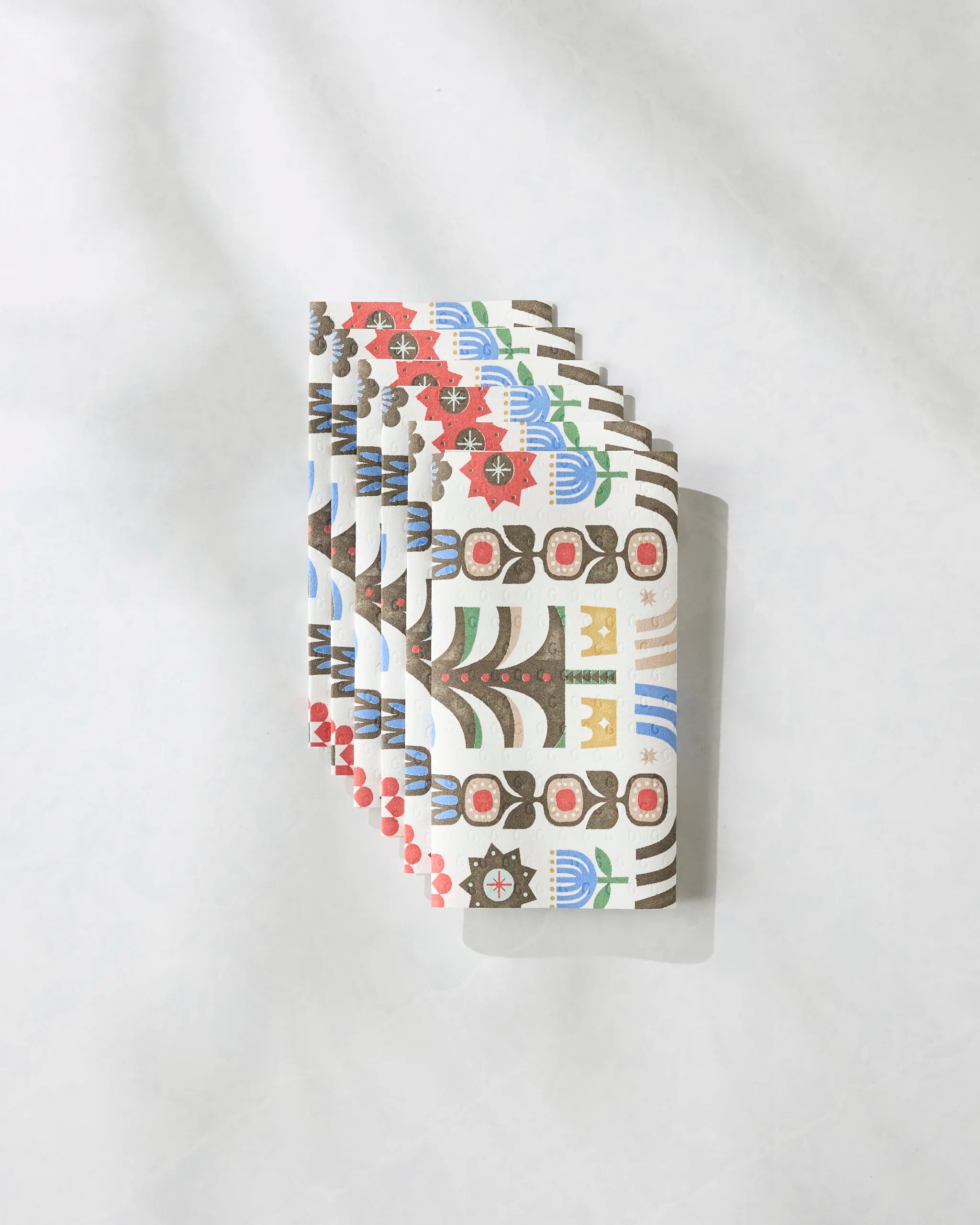 A fan of Everfolk playing cards by Geometry, featuring floral and abstract geometric designs in red, blue, green, yellow, and black, is displayed on a white textured surface inspired by vibrant eco-friendly kitchen towels.