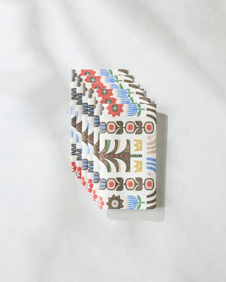 A fan of Everfolk playing cards by Geometry, featuring floral and abstract geometric designs in red, blue, green, yellow, and black, is displayed on a white textured surface inspired by vibrant eco-friendly kitchen towels.