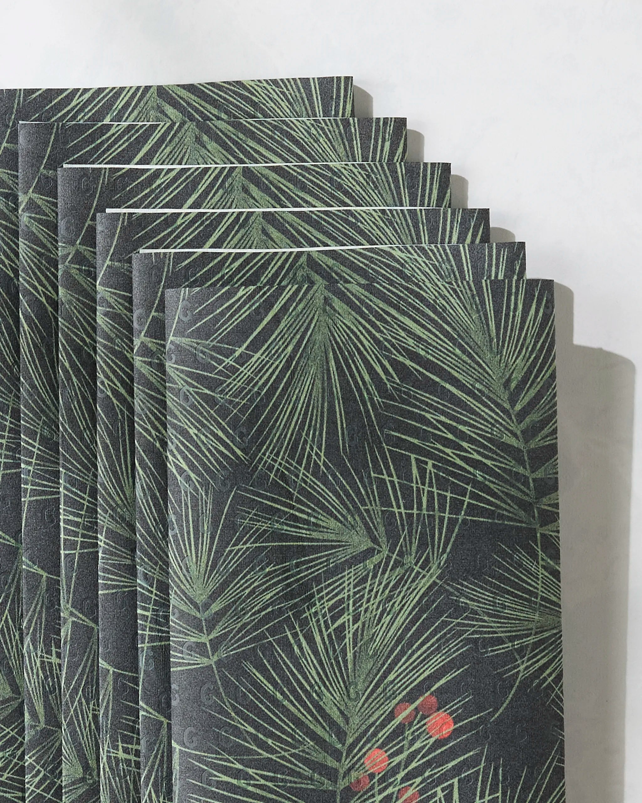 A stack of Geometry’s Evergreen Pine black envelopes, featuring a green pine needle and red berry design, fanned out on a marble surface—ideal for pairing with eco-friendly paper towels for festive, sustainable gifting.