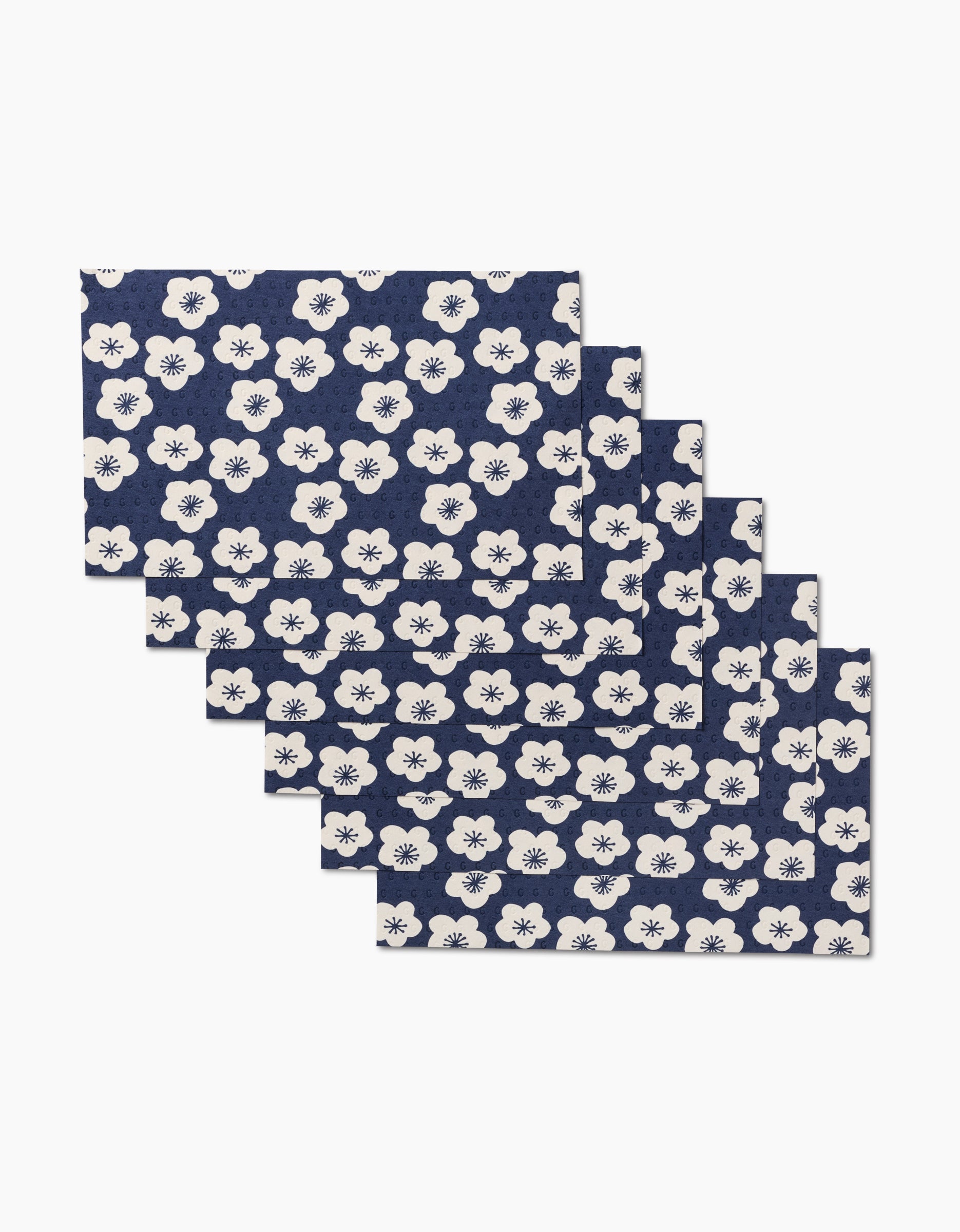 Six Every Sunday placemats by GEOMETRY in navy blue with a white floral pattern, fanned out for display—an eco-friendly, reusable alternative to disposable tableware.