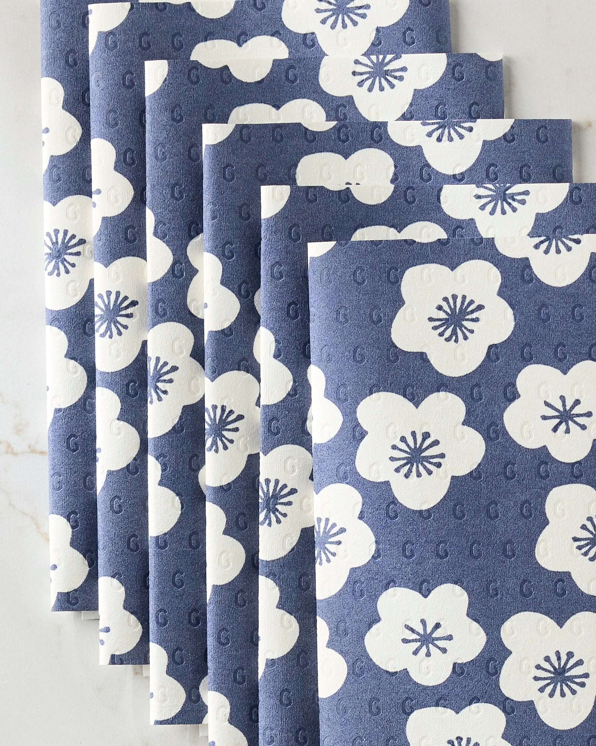 GEOMETRY’s Every Sunday reusable paper towels, featuring large white flowers with dark centers on a blue background, are neatly fanned out on a light surface.